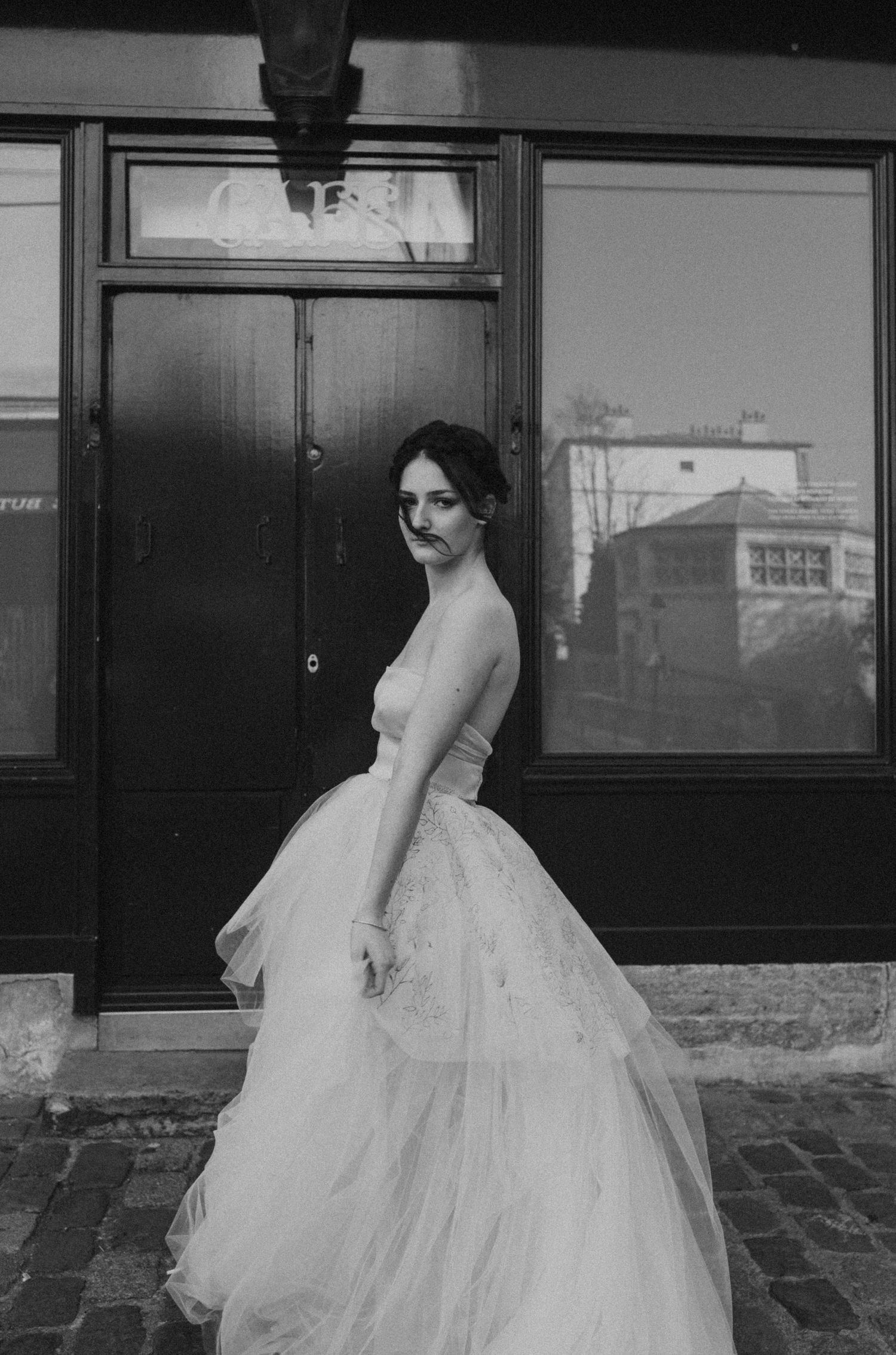 Black and white portrait of wedding dress with full tulle skirt against classic Parisian storefront.