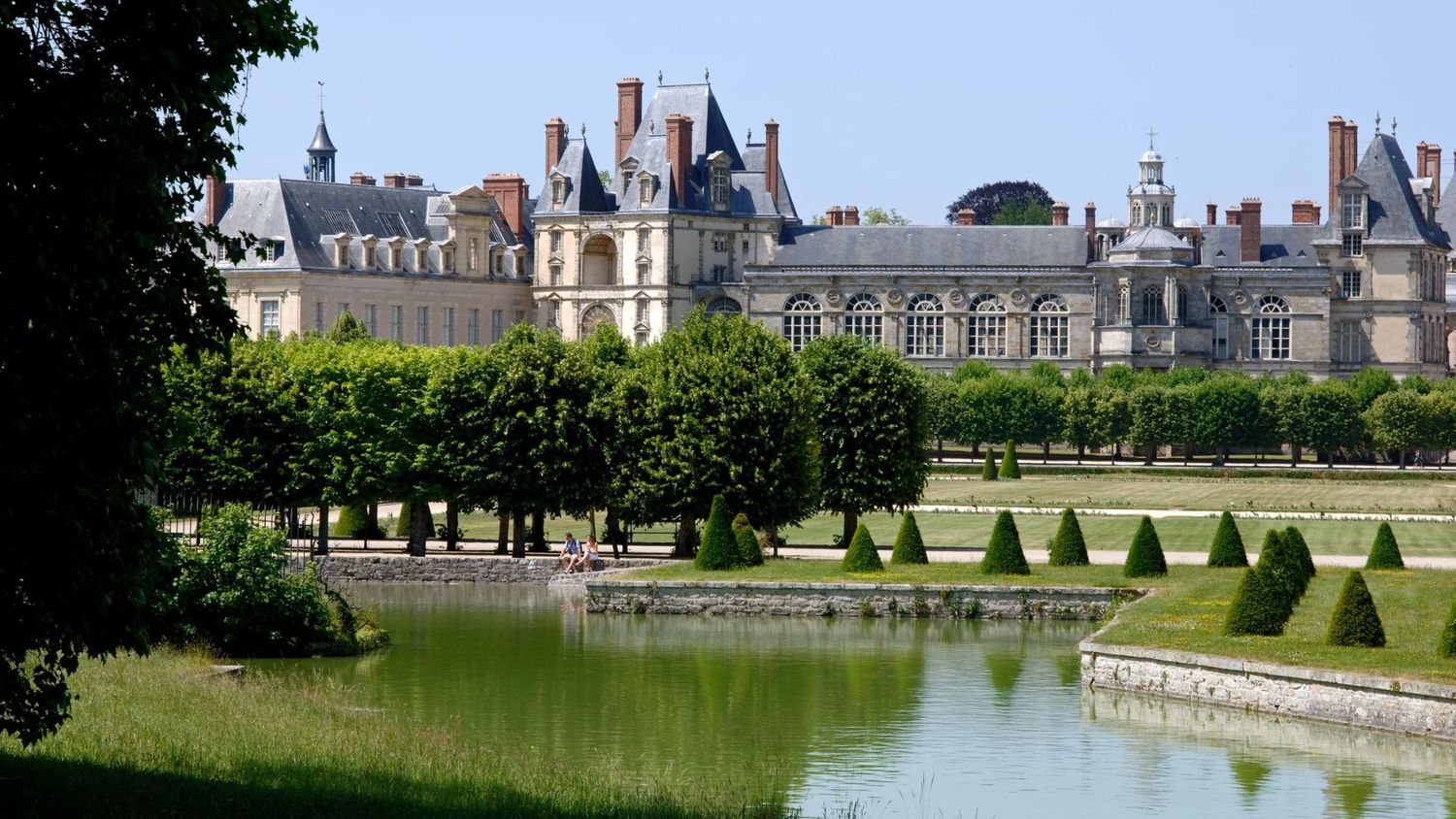Fontainebleau Palace with manicured gardens and reflecting pool on a sunny day.