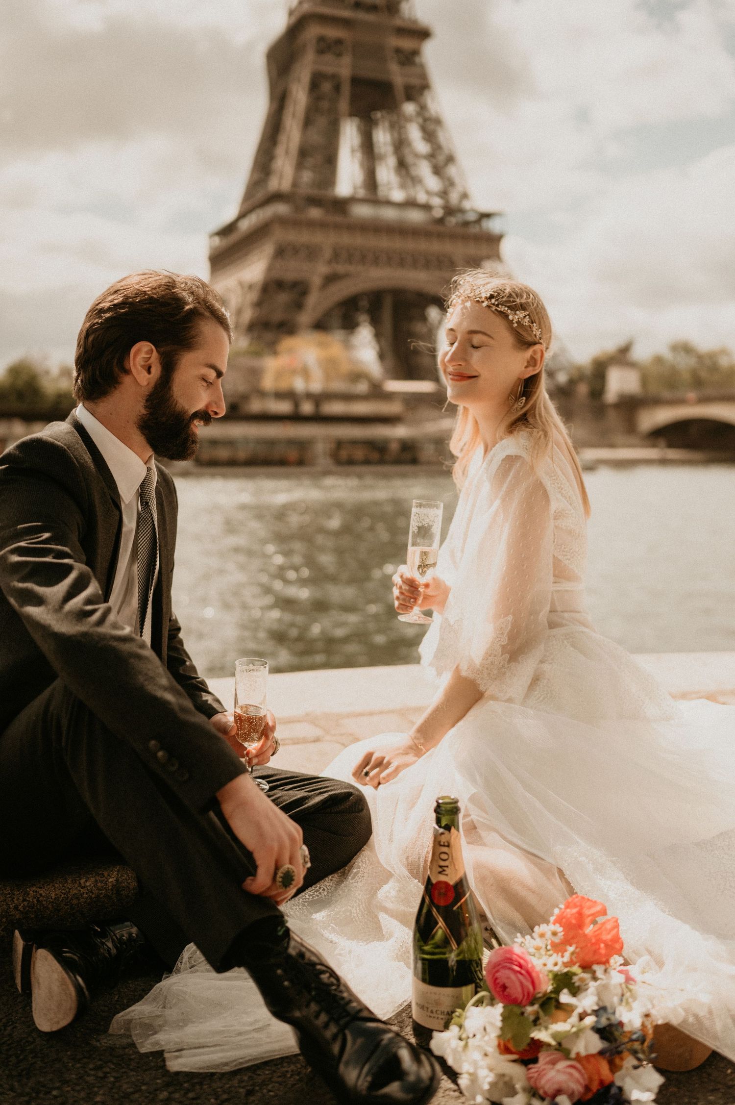 A wedding couple enjoys champagne and flowers along the Seine with the Eiffel Tower in background.