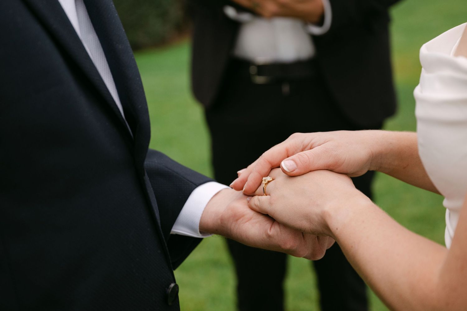 Close-up shot of hands exchanging wedding rings during an outdoor ceremony.