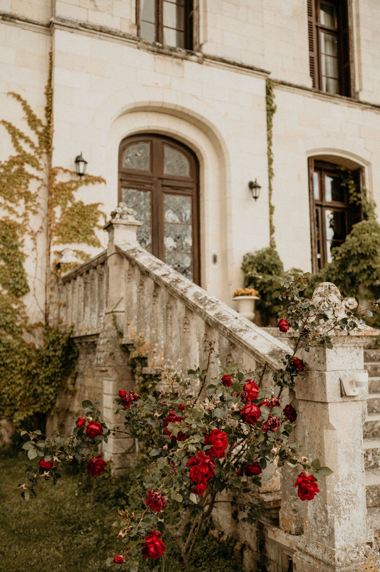 Stone staircase entrance to elegant building with blooming red roses climbing along railing.