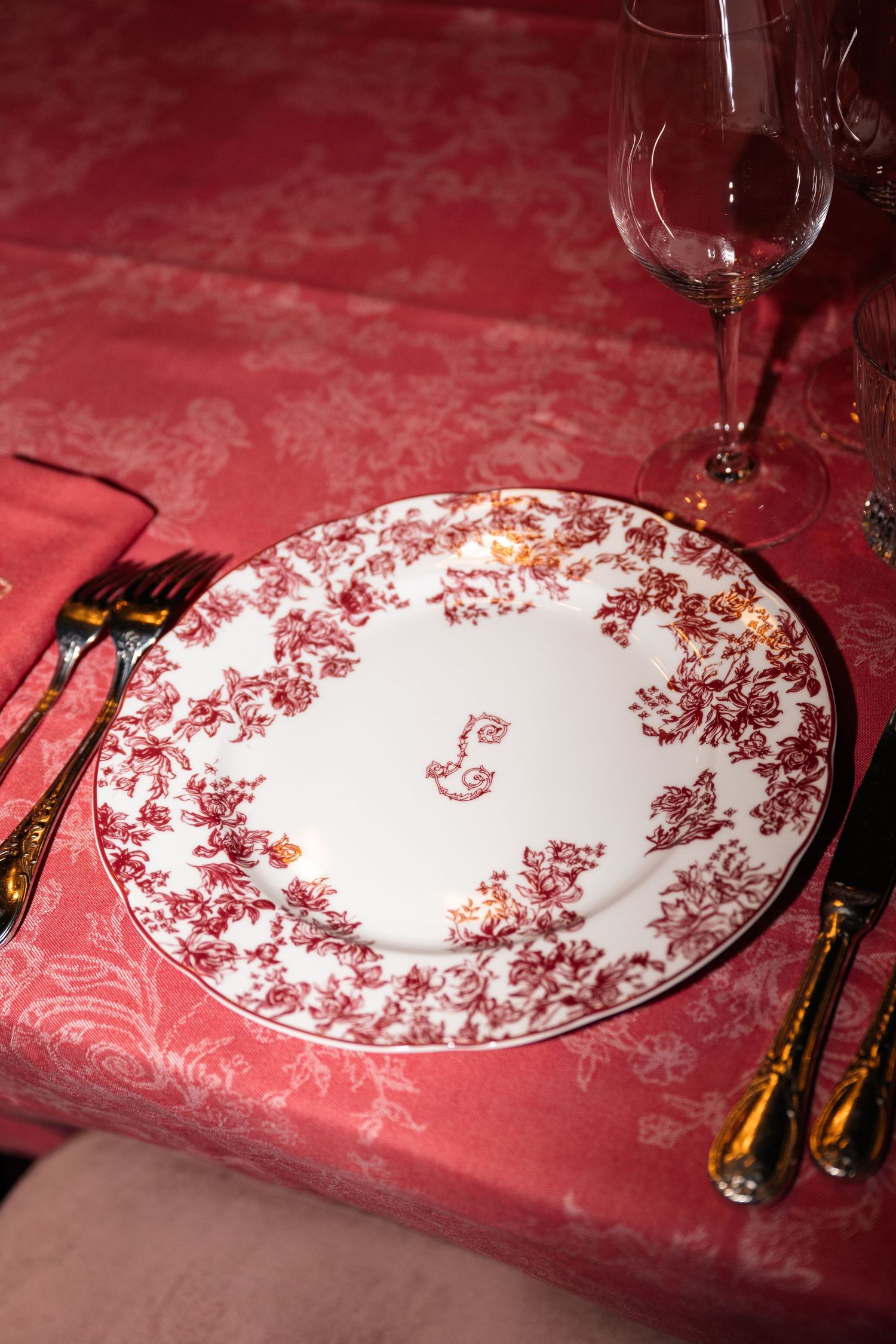 Elegant red floral china place setting with gold cutlery on a red damask tablecloth.
