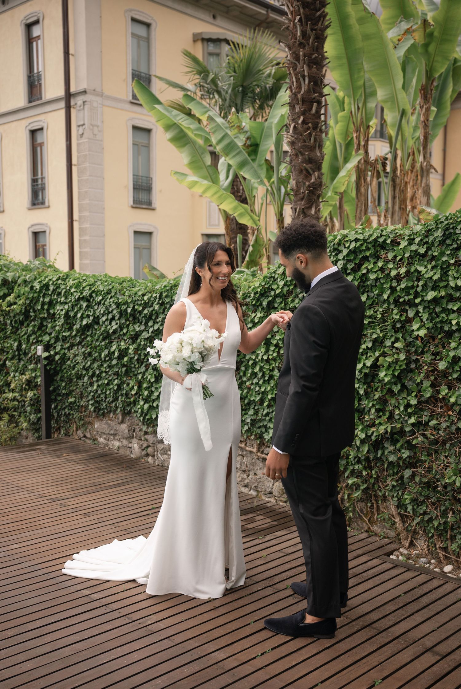 Bride and groom sharing first look moment on wooden deck surrounded by lush greenery at Lake Como wedding.