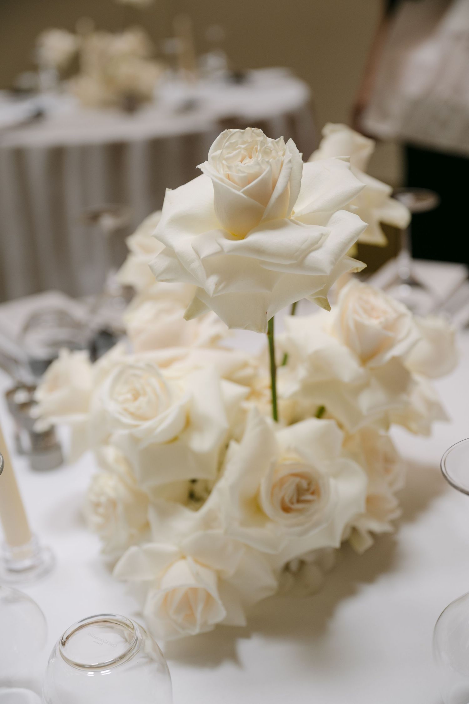 Elegant white rose centerpiece with a single tall rose at a wedding reception table.