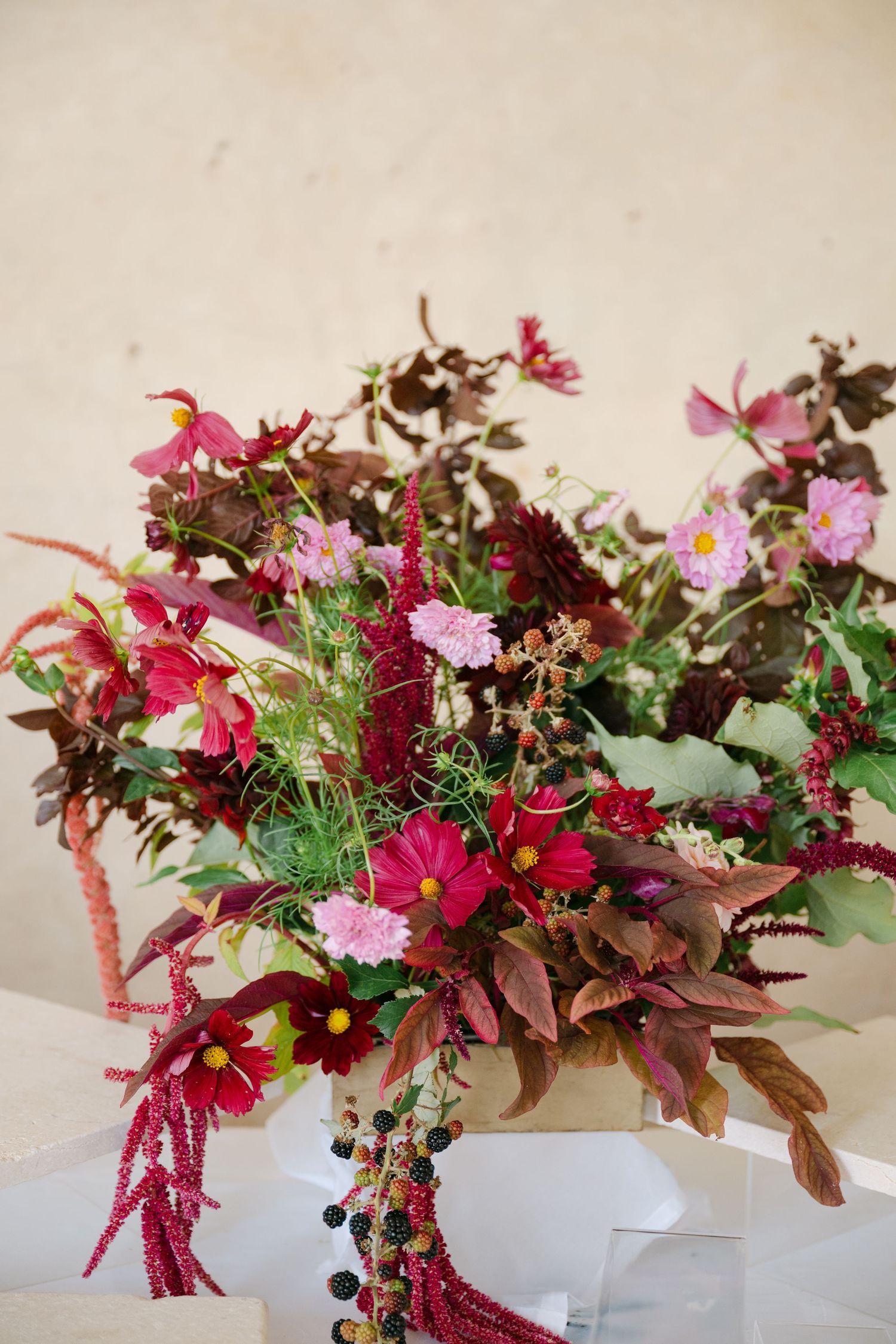 Rich burgundy and pink wildflower wedding bouquet with amaranthus and cosmos in a white vase.