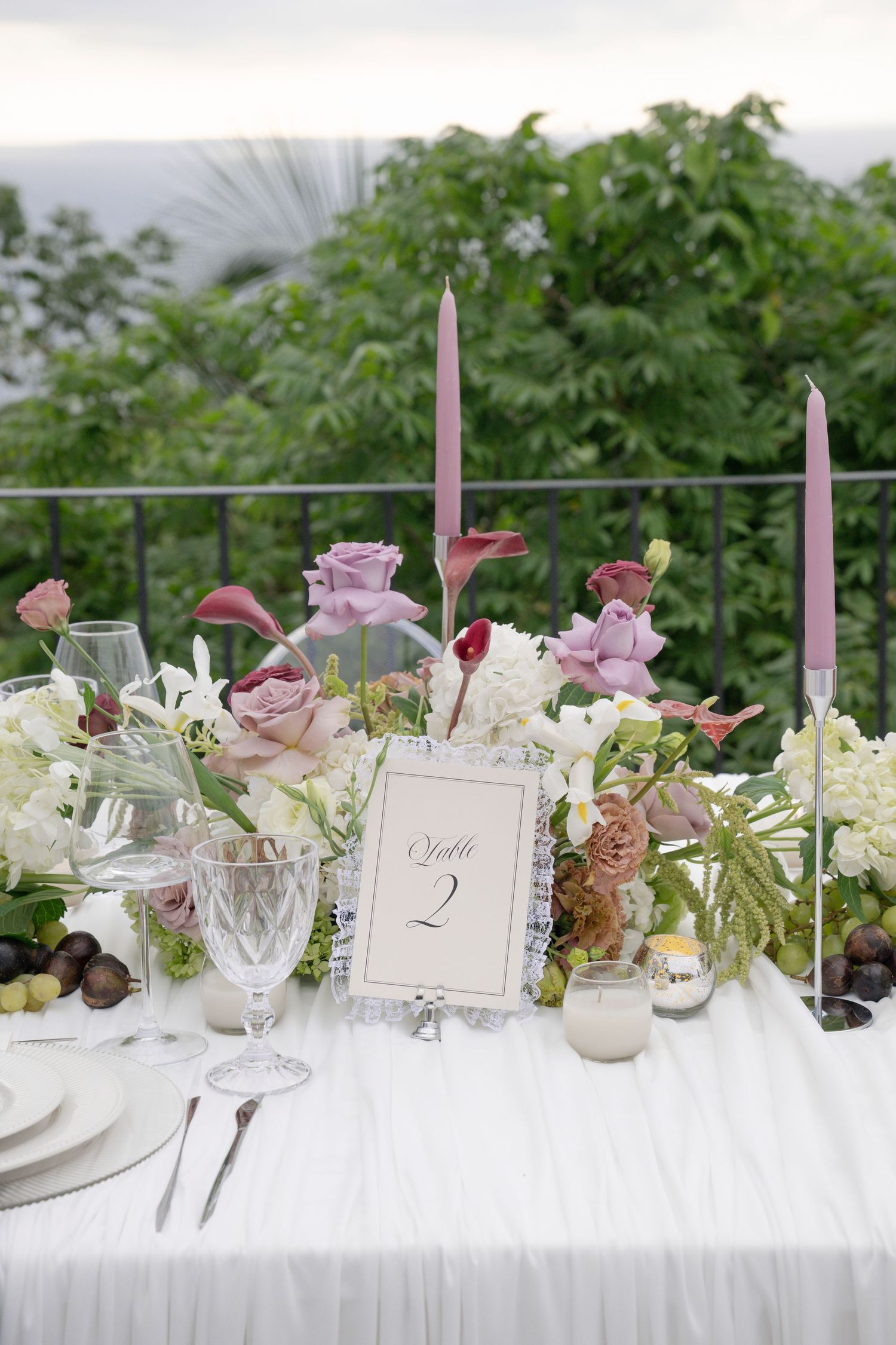 Outdoor wedding reception table with mauve roses, purple taper candles, and Table 2 number card.