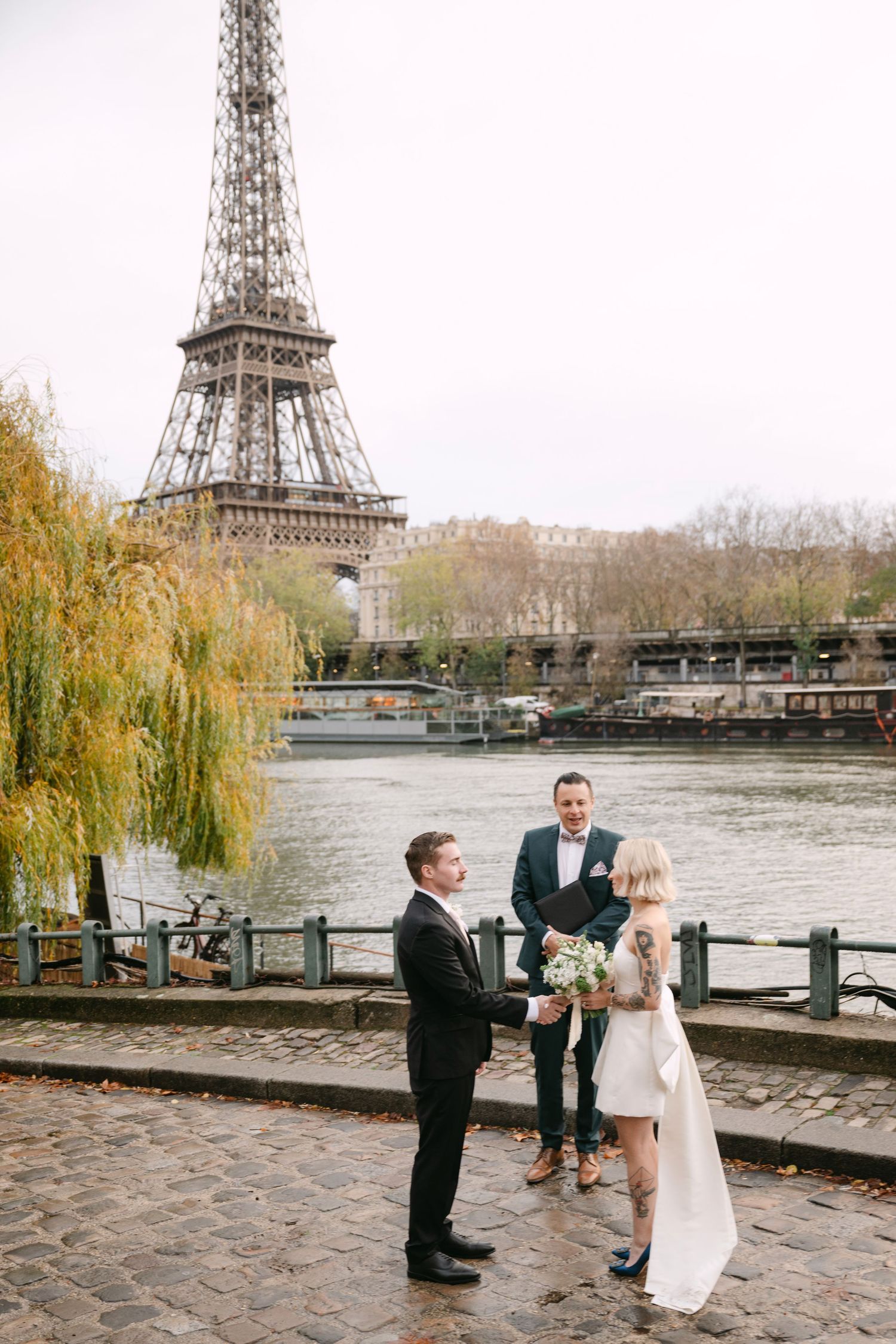 Couple exchanging vows in an intimate elopement ceremony beside the Seine River with Eiffel Tower backdrop.