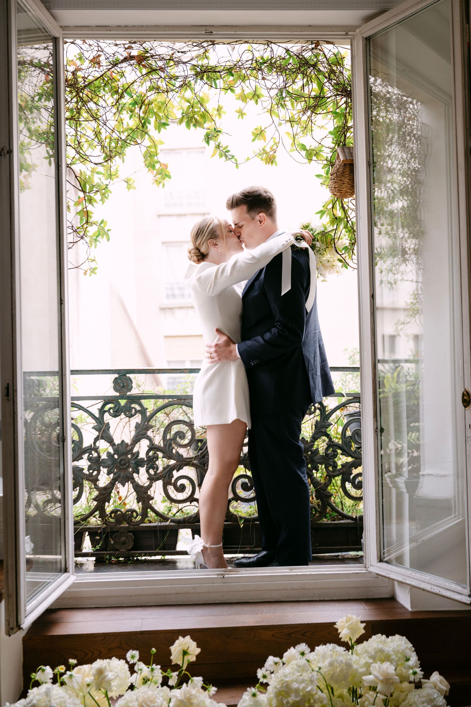A romantic moment on a Parisian-style balcony with white flowers and green vines framing the French doors.