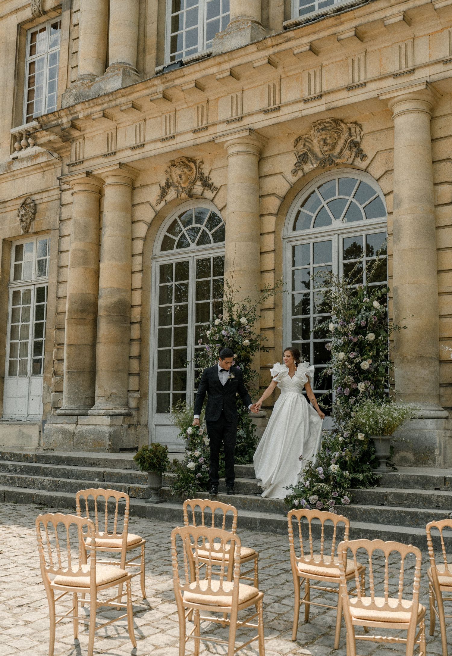 Elegant wedding ceremony setup outside a French chateau with wooden chairs and floral arrangements.