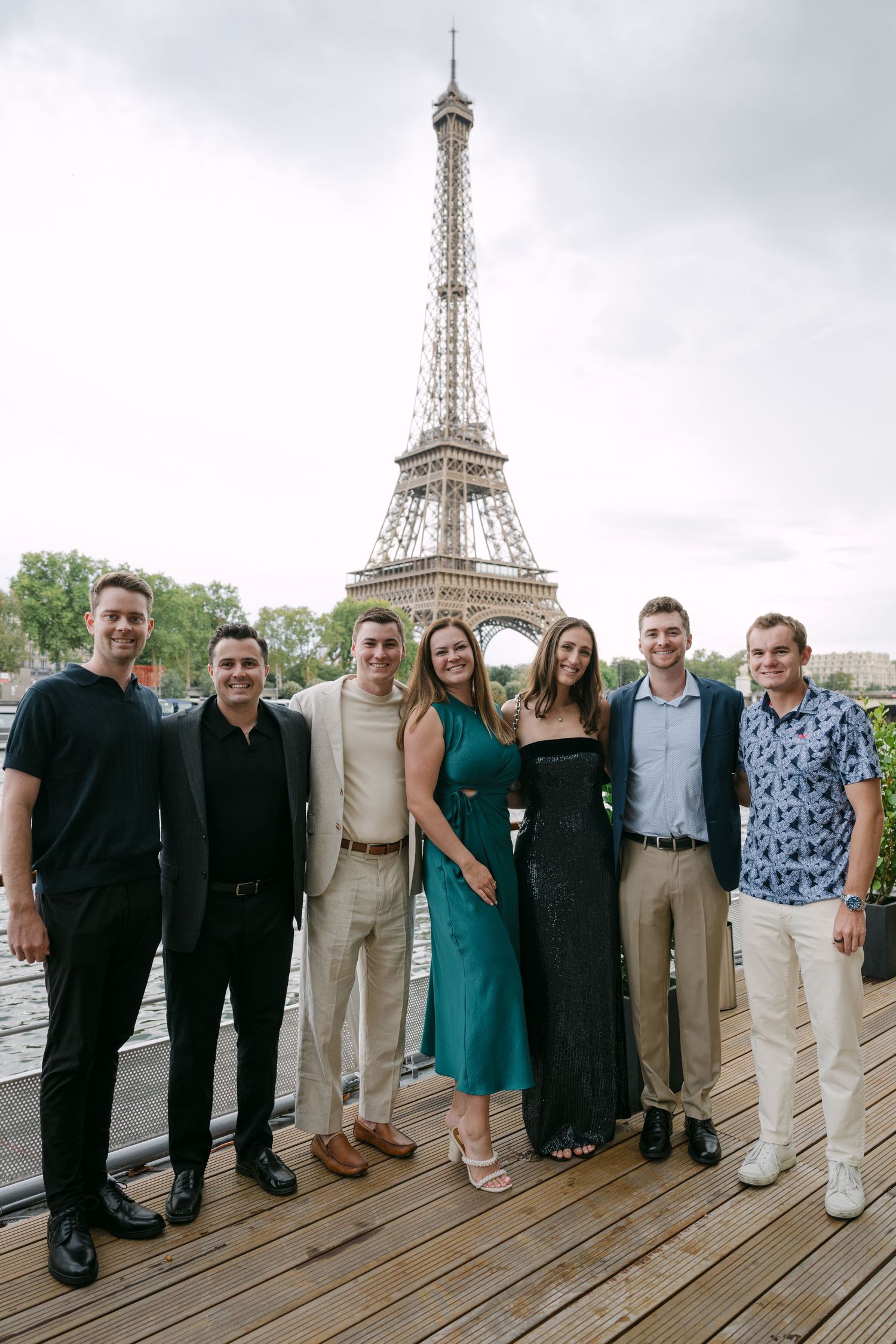 Group of friends posing together on a wooden deck with the Eiffel Tower visible in the background.
