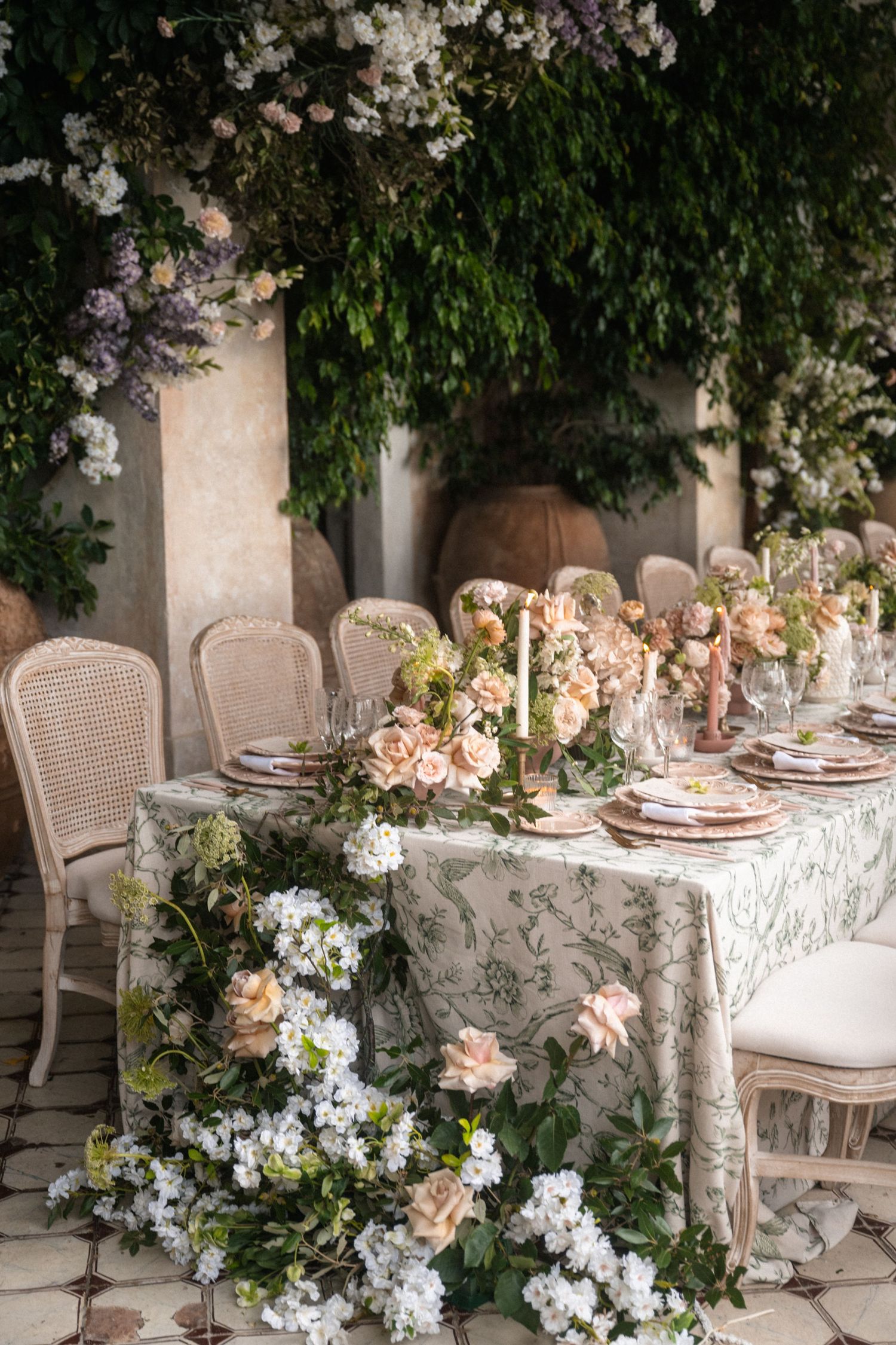 Romantic outdoor wedding reception table adorned with blush roses, candles, and lush greenery decor.