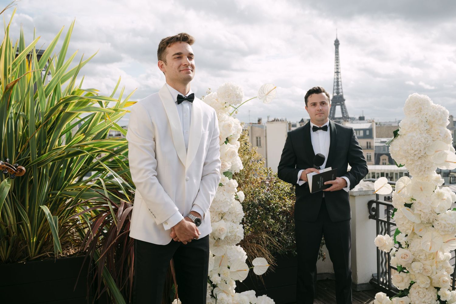 A formal event scene with elegant white orchids and tuxedo-clad attendees against a cloudy outdoor backdrop.