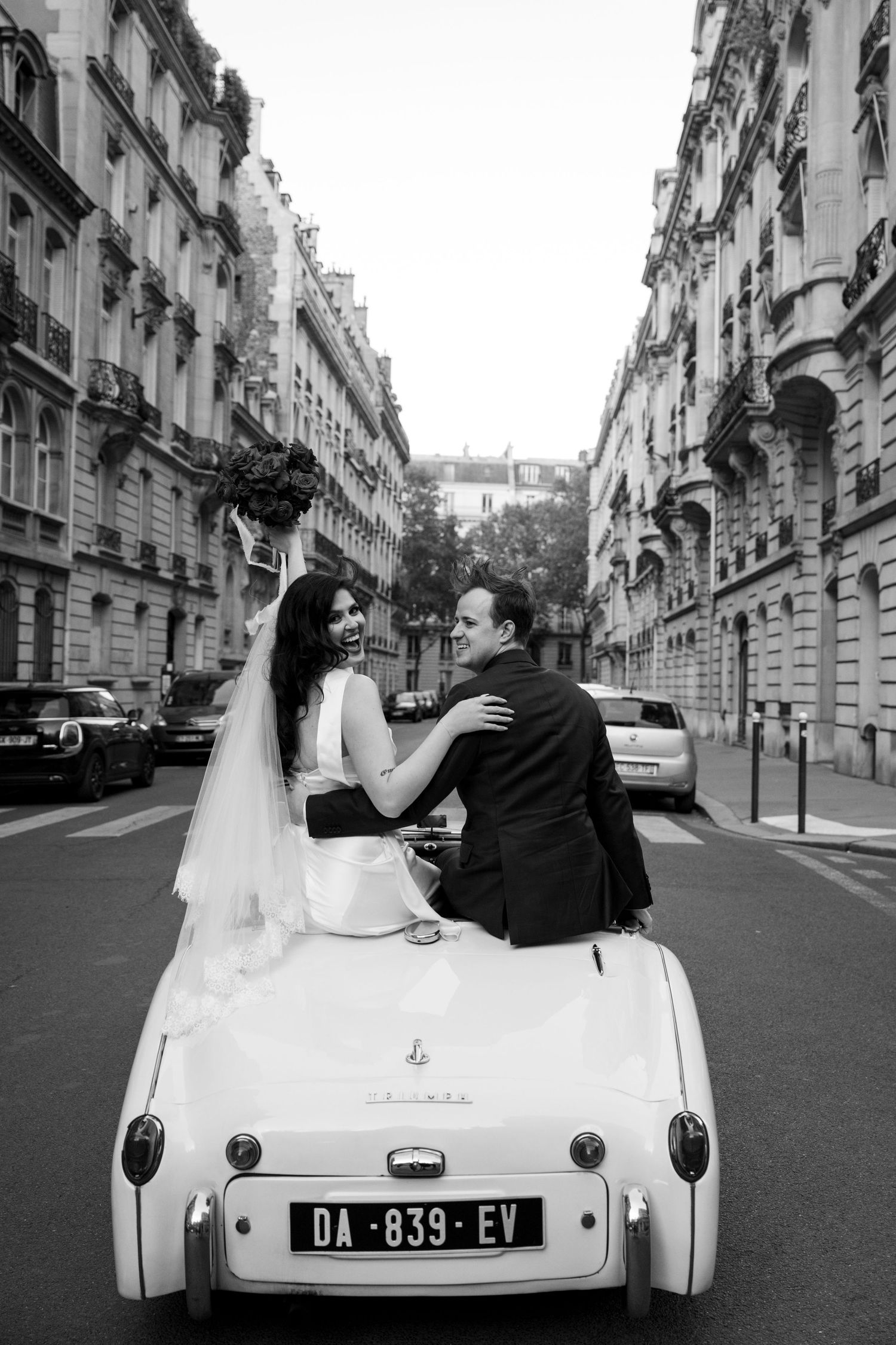 A couple sits in a vintage white car on a classic Parisian street in a series of romantic black and white photos.