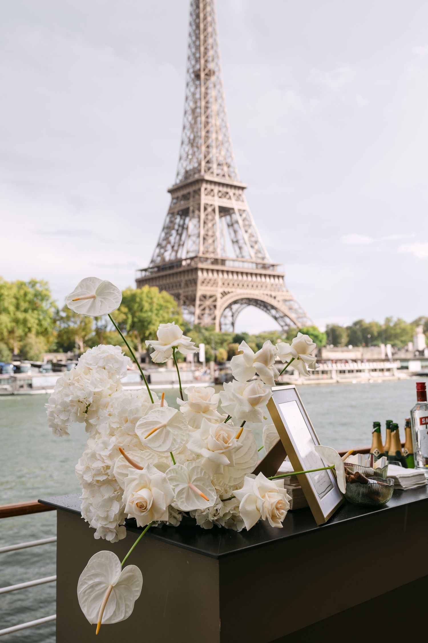 White floral arrangement with roses and anthuriums on a bar with the Eiffel Tower visible in the background.