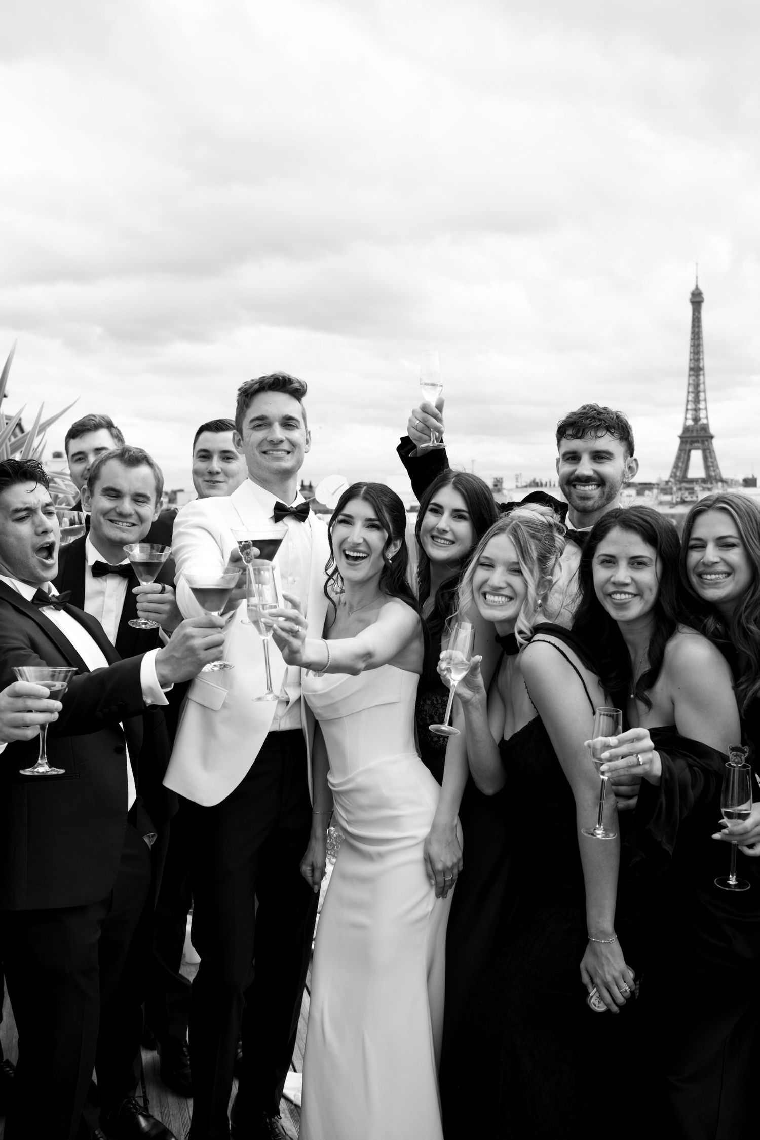 Black and white photo of a wedding party toasting with champagne in front of the Eiffel Tower in Paris.