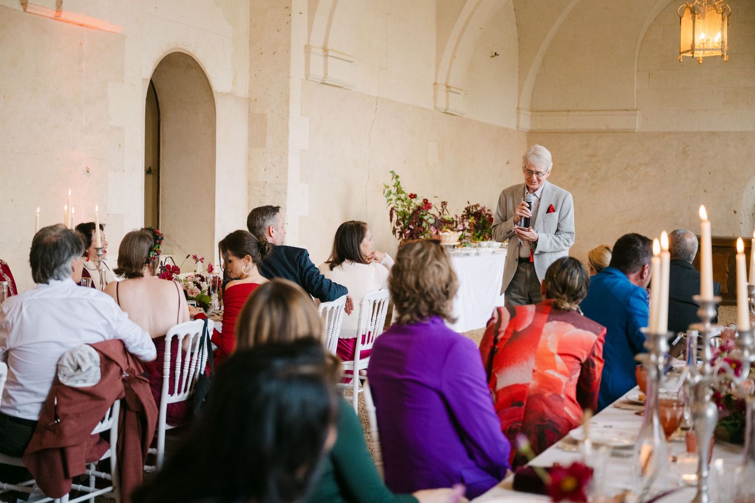 Man giving a speech at an elegant wedding reception in a vaulted stone hall.