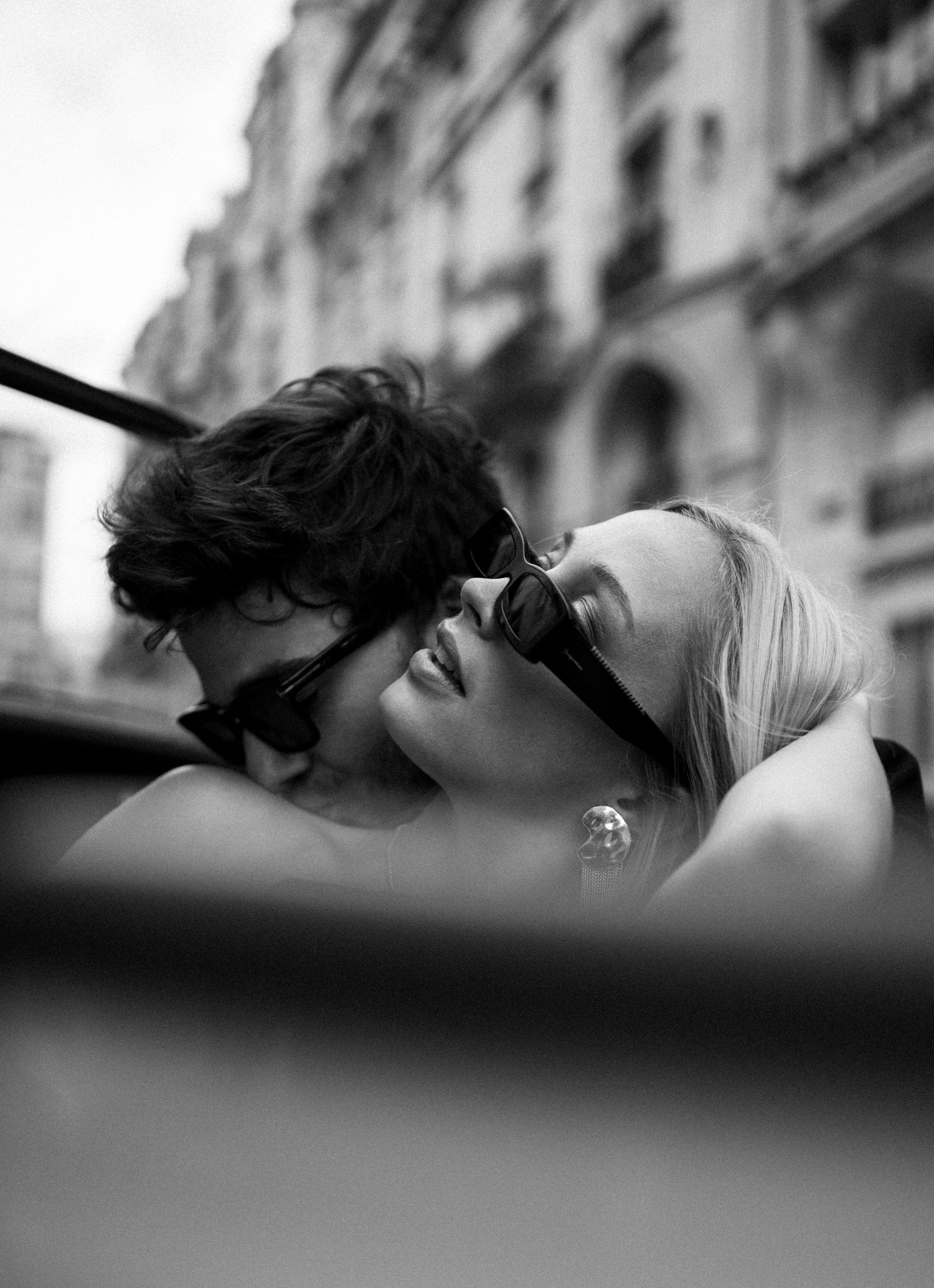 Black and white photo of bride and groom sharing a kiss in vintage convertible on Paris street.