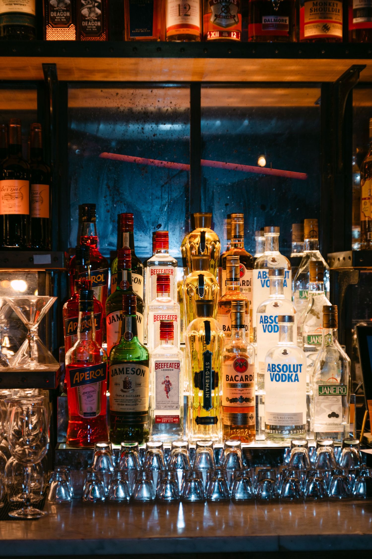 Well-stocked bar shelf featuring Absolut Vodka, Jameson, Aperol, and Bacardi bottles.