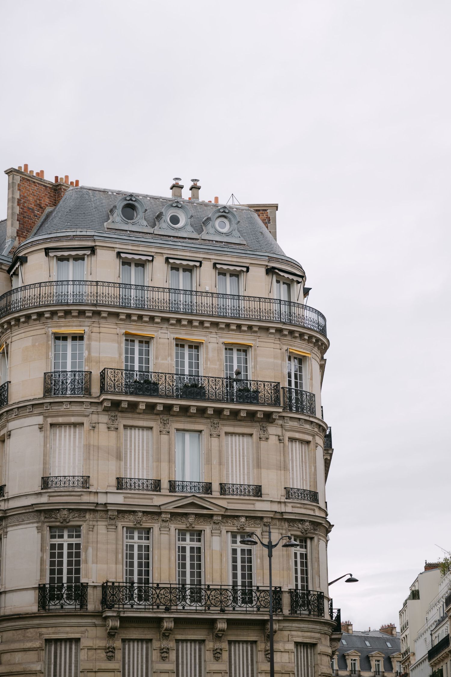 Classic Haussmann-style Parisian apartment building facade with ornate balconies under cloudy sky.