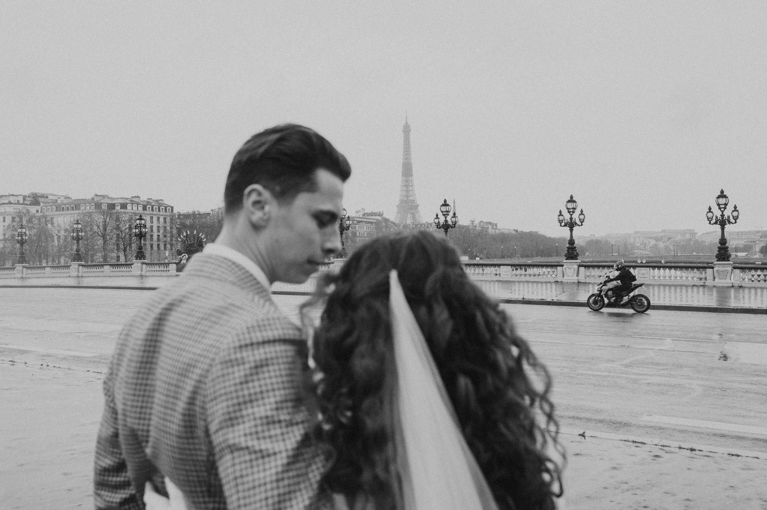 Couple in wedding attire looking out over Seine River with Eiffel Tower in distance.
