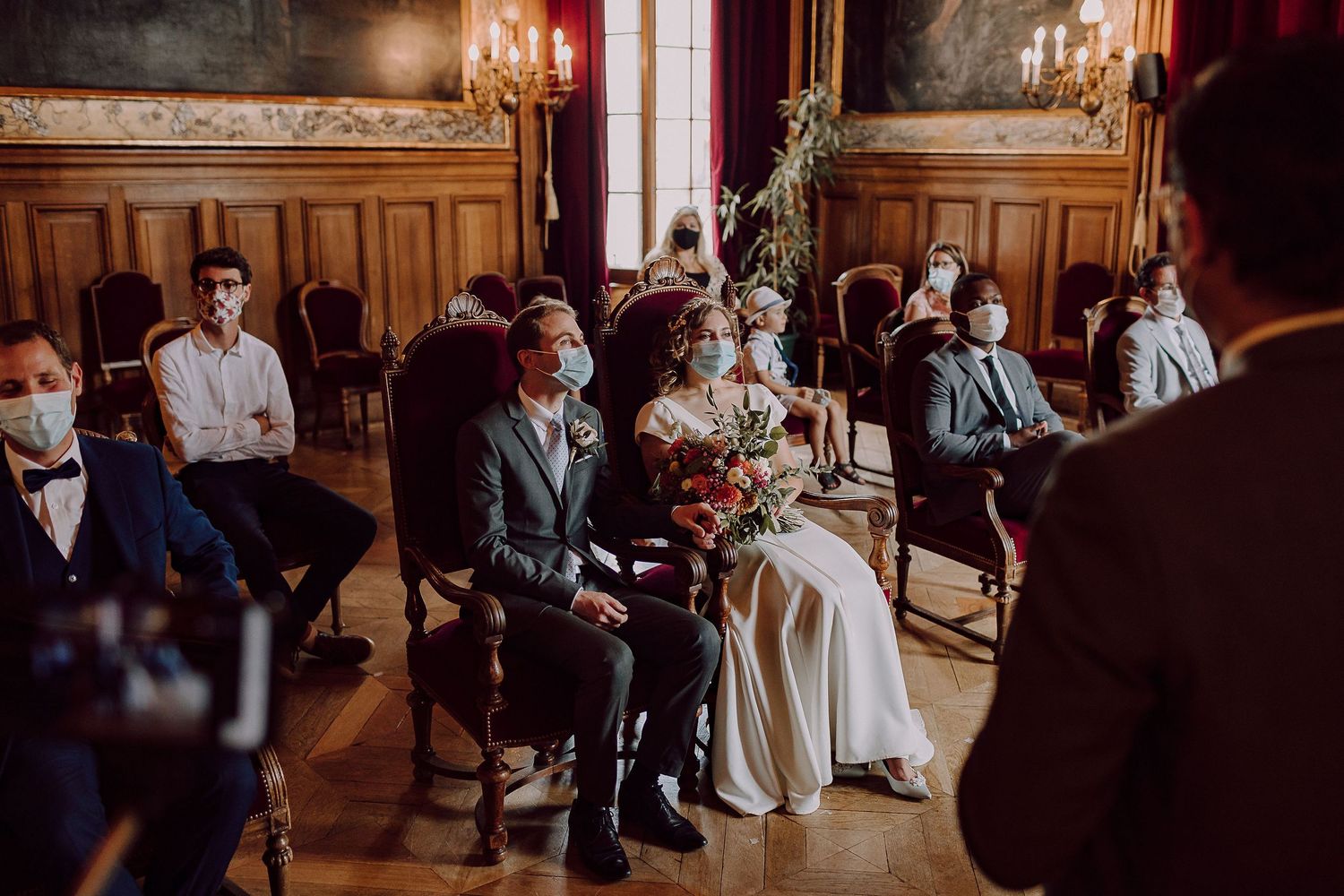 Indoor wedding ceremony in an elegant room with wood paneling and chandeliers.