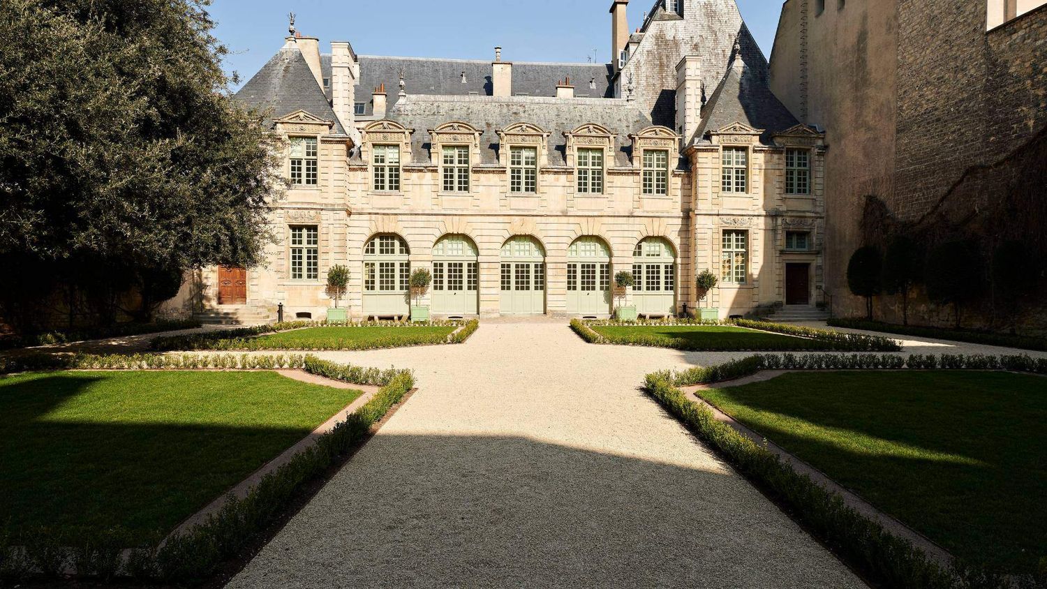 Elegant French mansion with arched windows and manicured garden paths leading to grand entrance.