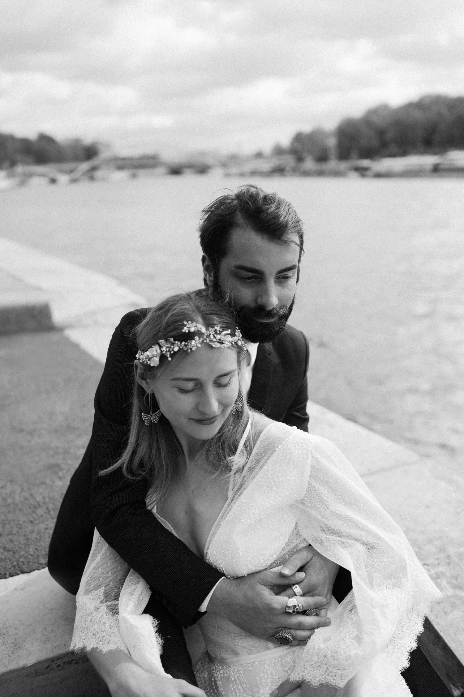 Black and white portrait of newlyweds sharing tender moment by Parisian waterfront.