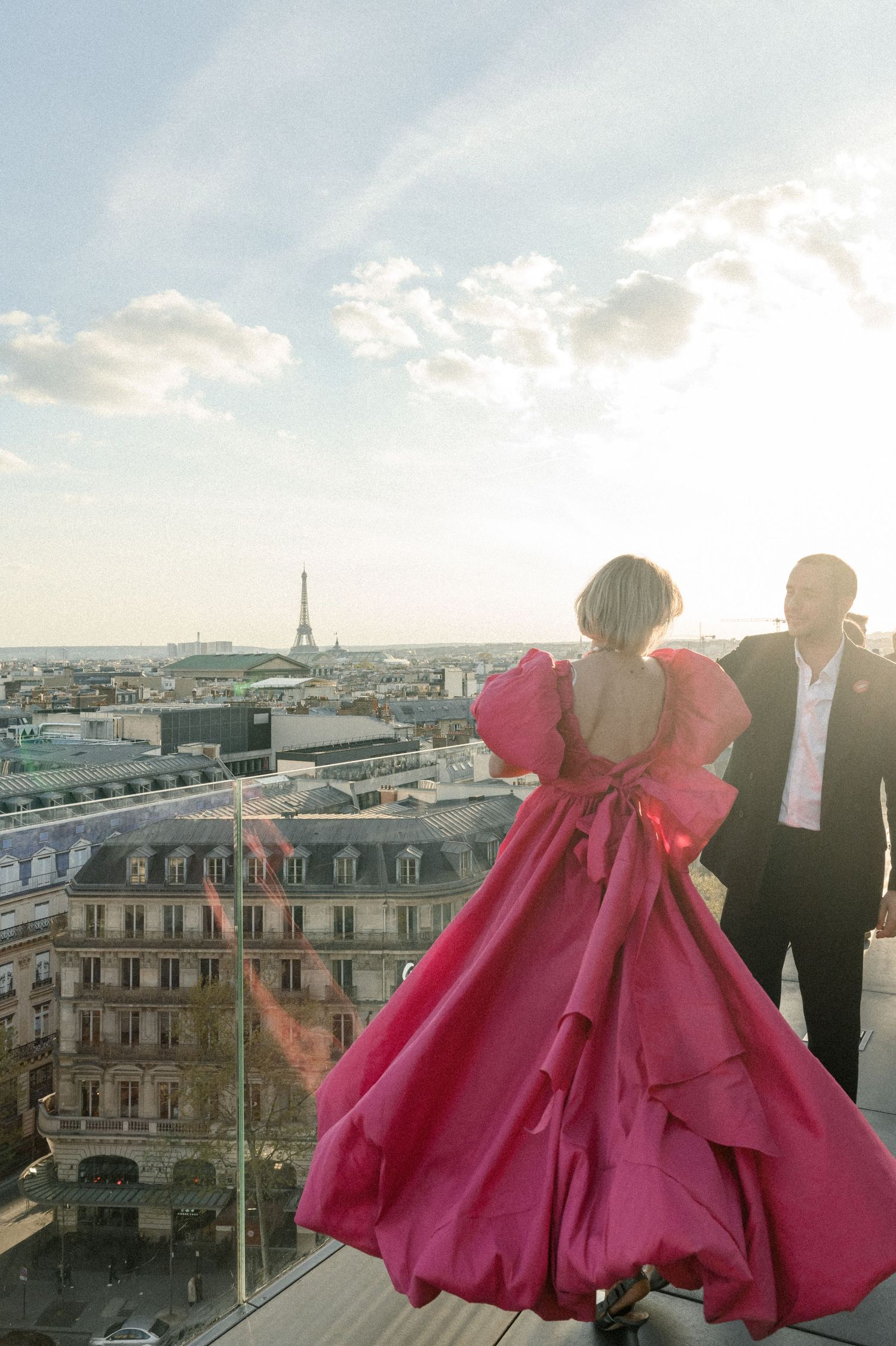 A dramatic pink gown flows in the breeze on a Parisian rooftop with the Eiffel Tower in view.