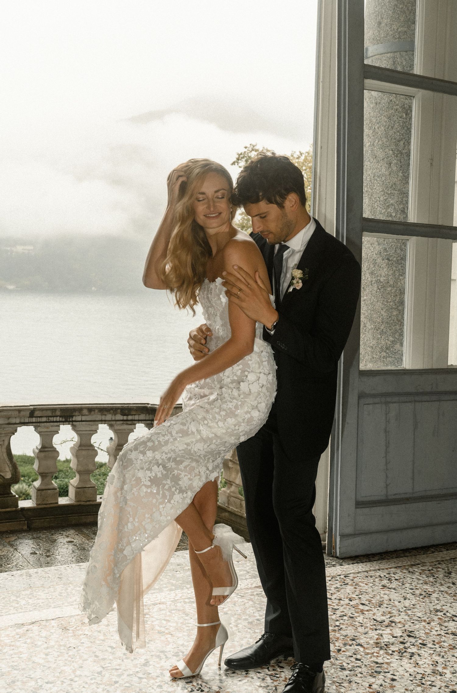 Elegant couple sharing a romantic moment by a window overlooking a scenic lake view.