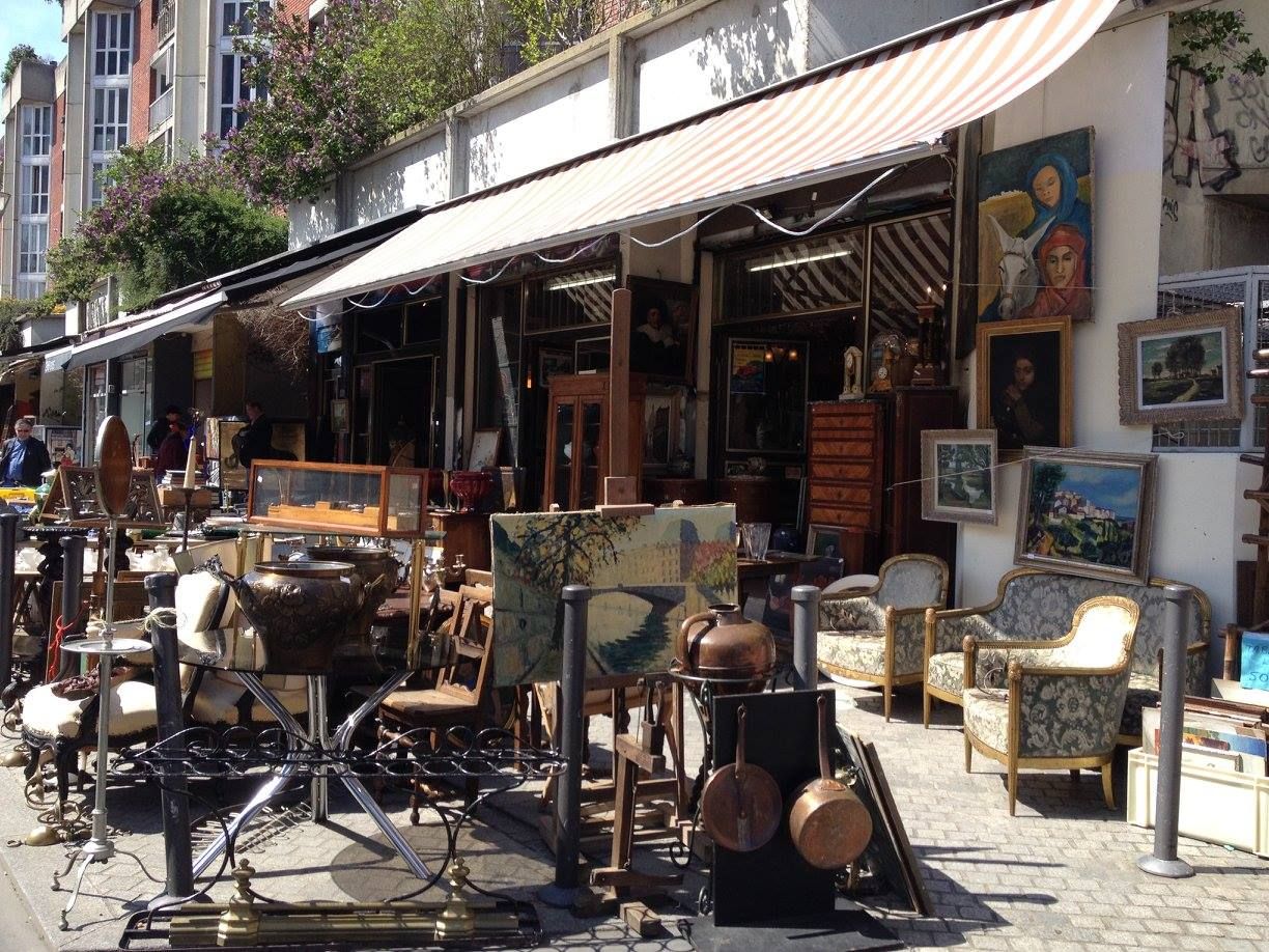 Antique market stall displaying vintage furniture and artwork on a sunny street in Paris.