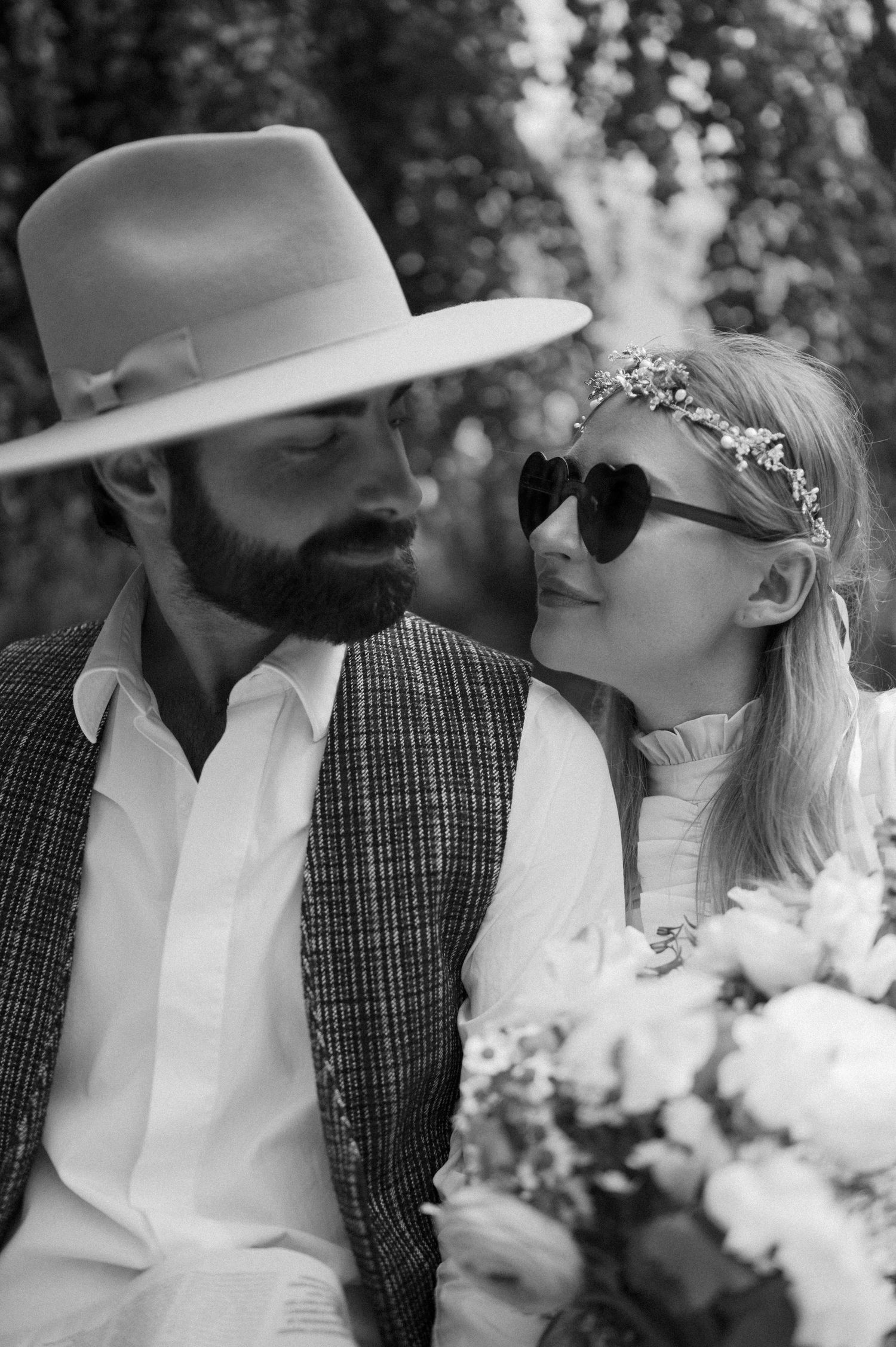 A romantic black and white photo of a couple in vintage attire with a fedora hat and sunglasses.