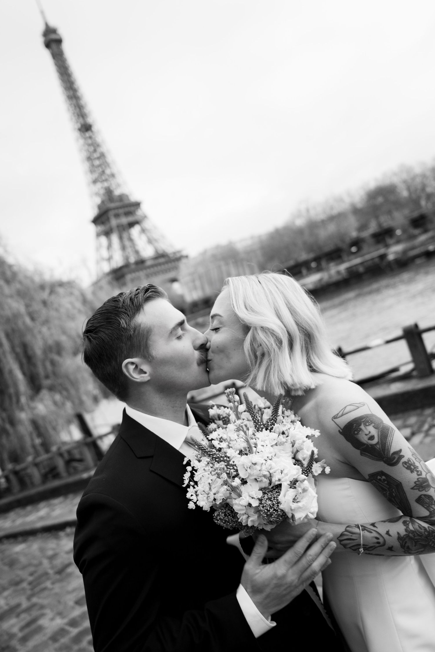 Bride and groom sharing a romantic kiss in black and white portrait near the Eiffel Tower in Paris.