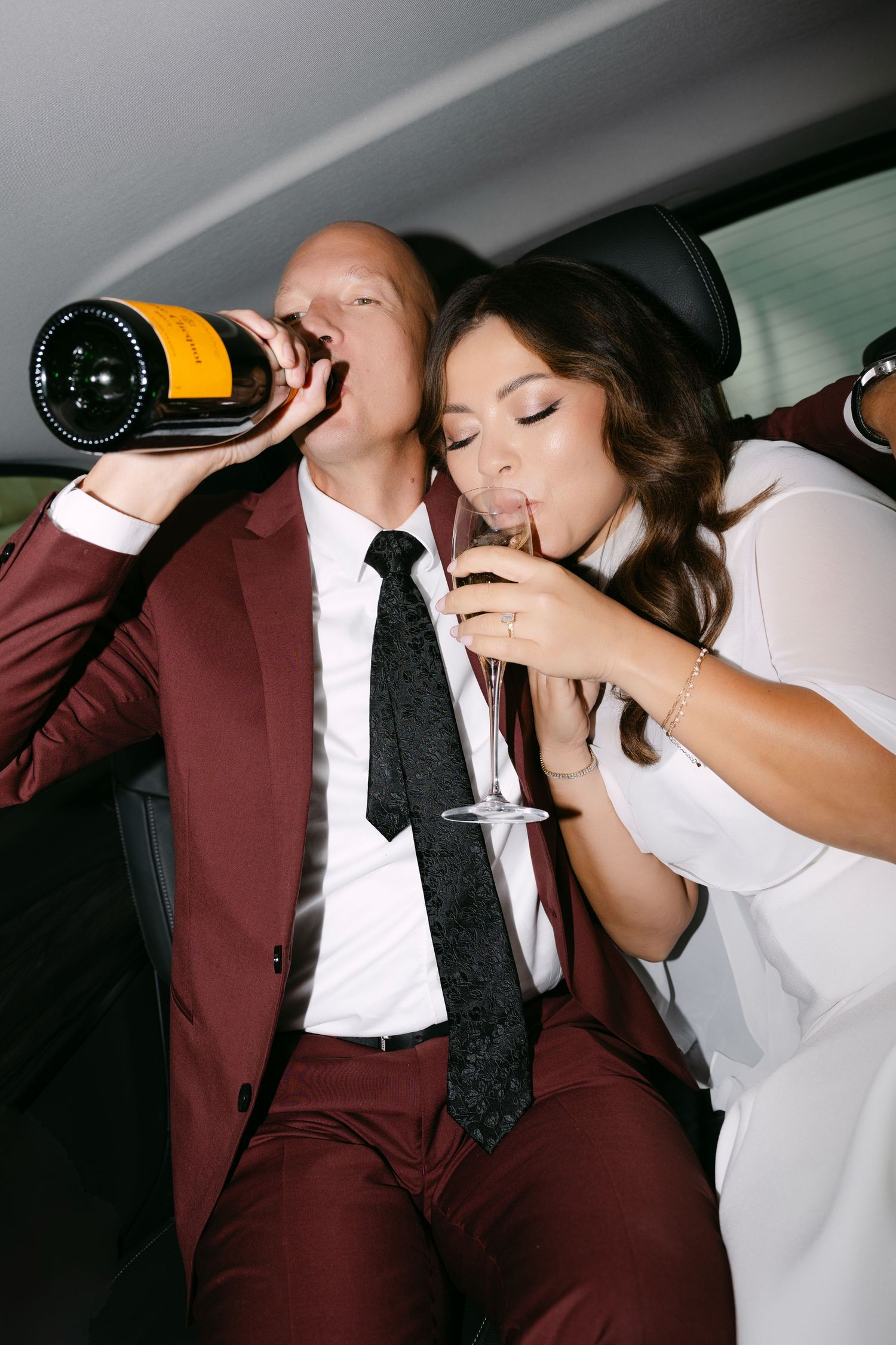Bride and groom drinking champagne together in a limousine after their wedding ceremony.