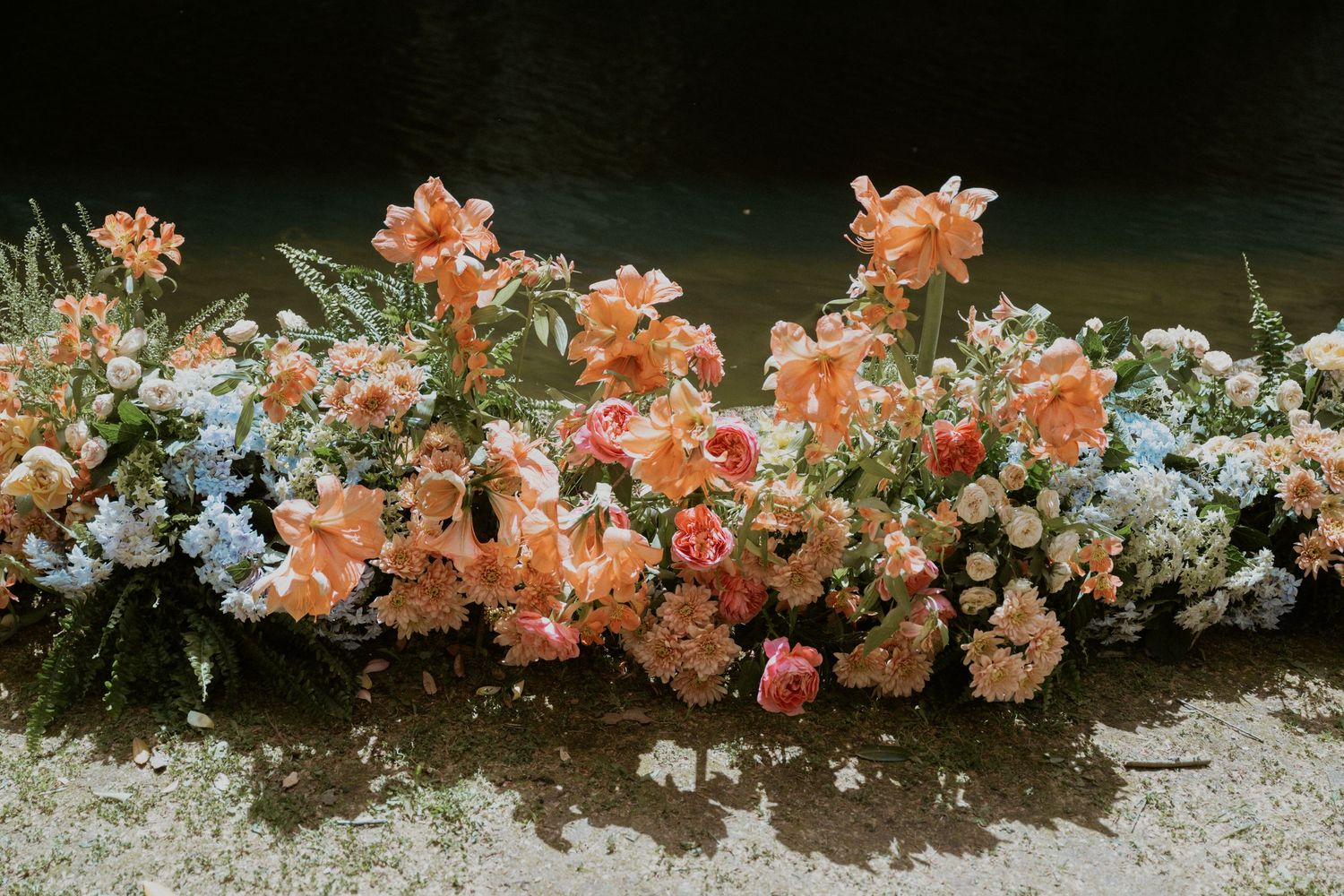 Lush floral arrangement featuring peach, pink, and blue flowers displayed outdoors near water.