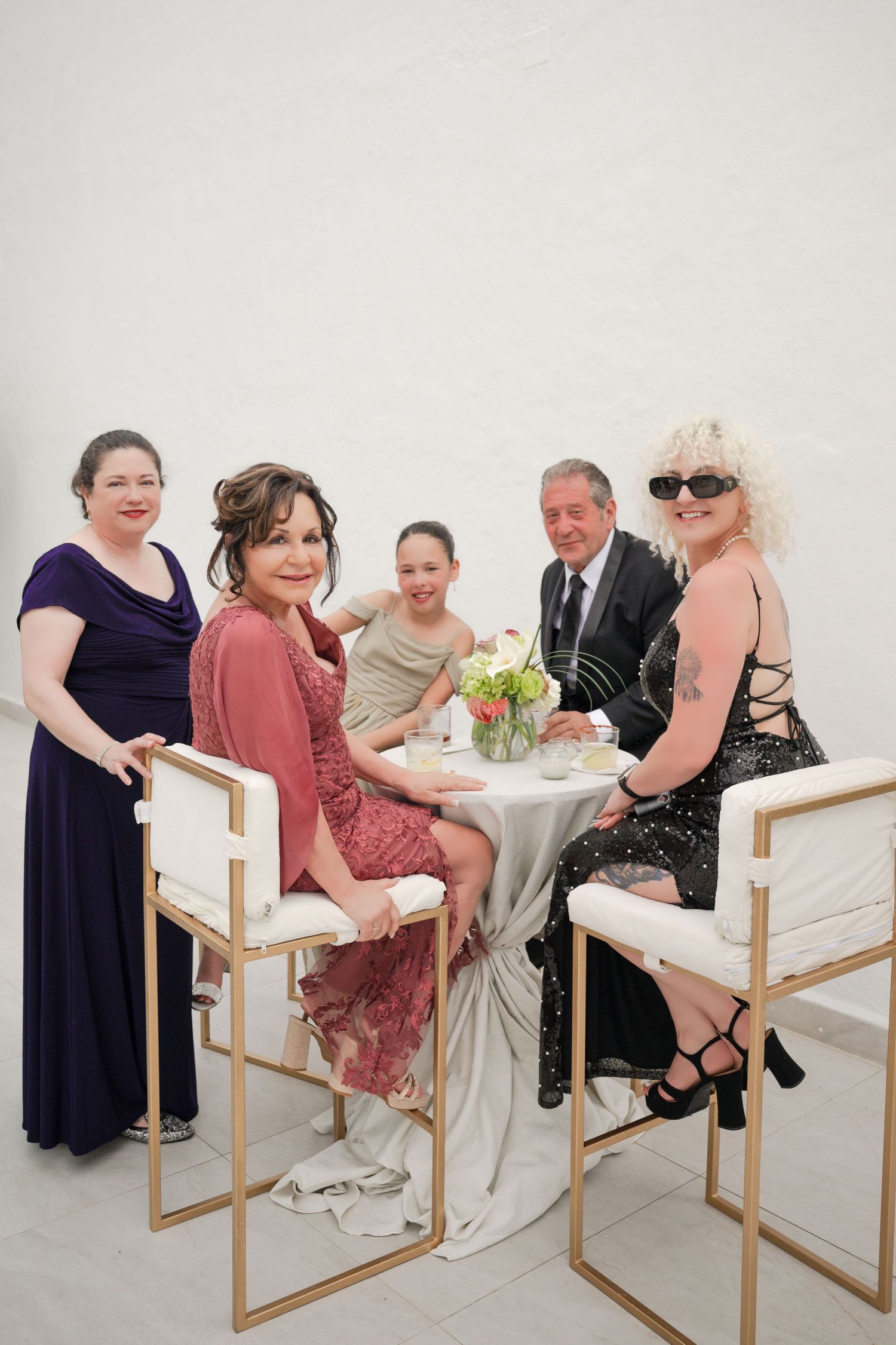 Five elegantly dressed guests pose together at a white and gold table during a formal event or wedding reception.