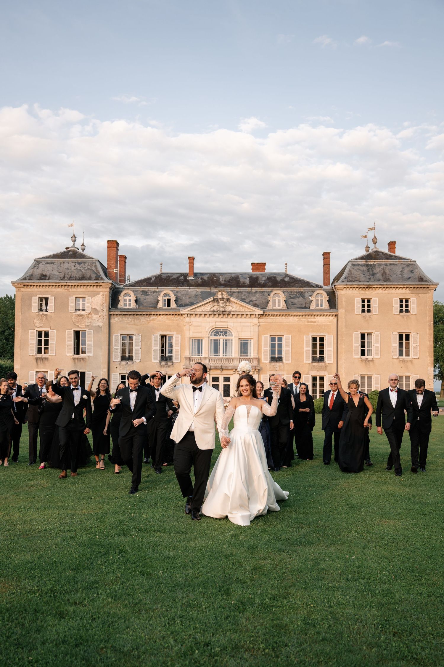 Wedding celebration on the lawn of a grand French chateau with formal gardens and classical architecture.