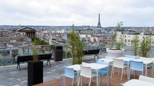 Modern rooftop dining area in Paris with blue and white furniture overlooking the cityscape.