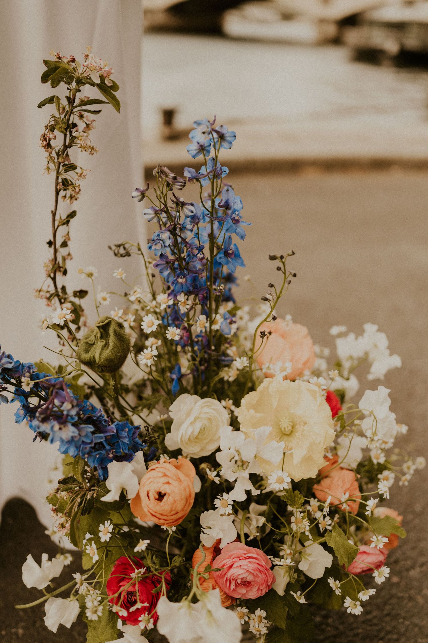 Elegant floral arrangement featuring blue delphiniums, roses, and white flowers in vintage style.