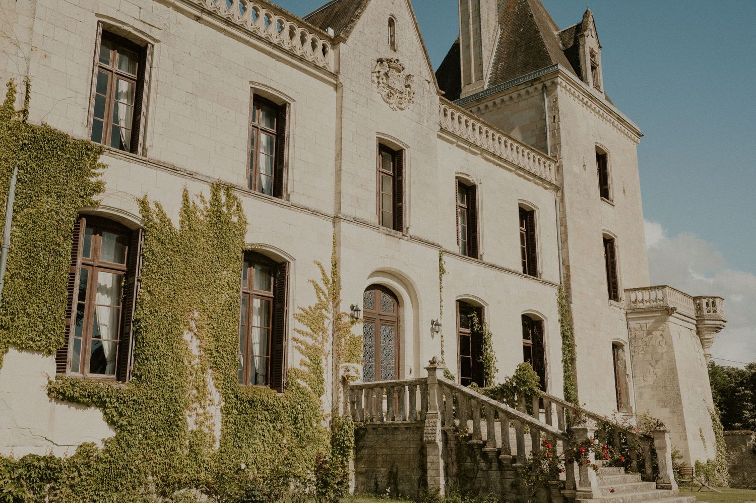 Historic French chateau with ivy-covered walls and grand stone staircase entrance.