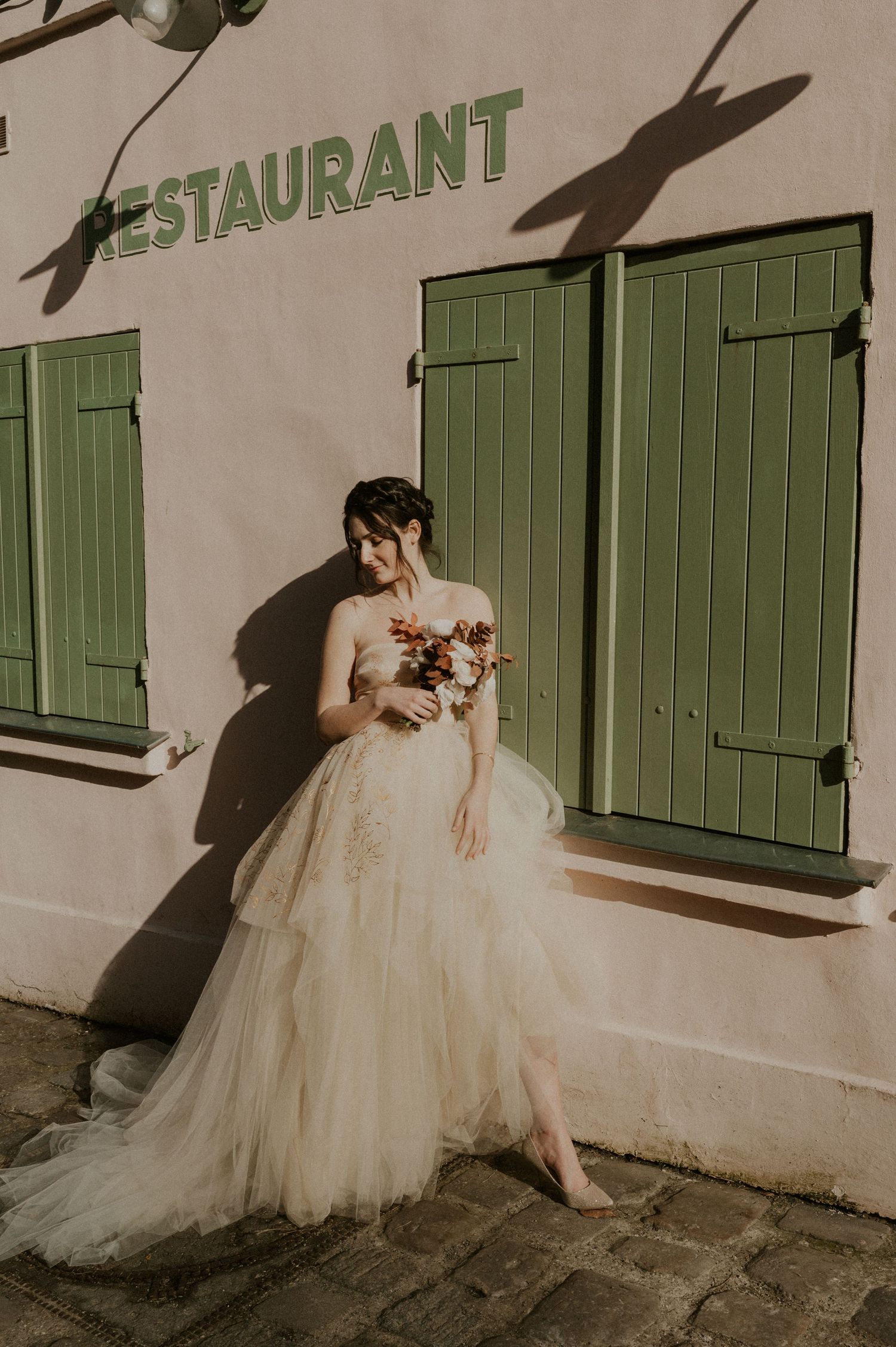Wedding dress photography against a pink wall with green shutters at a French restaurant.