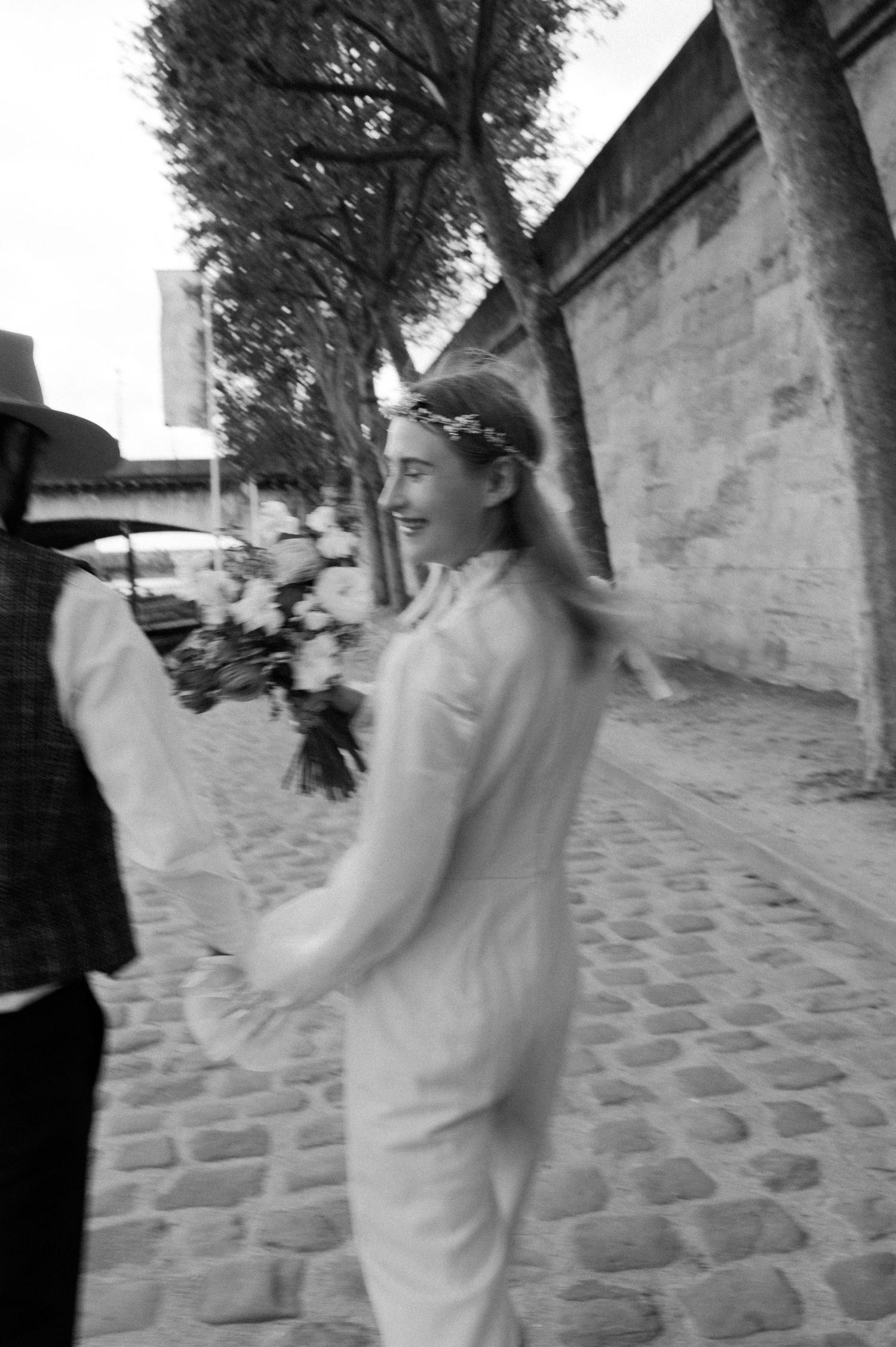 A black and white candid moment of a bride holding flowers on a cobblestone path.