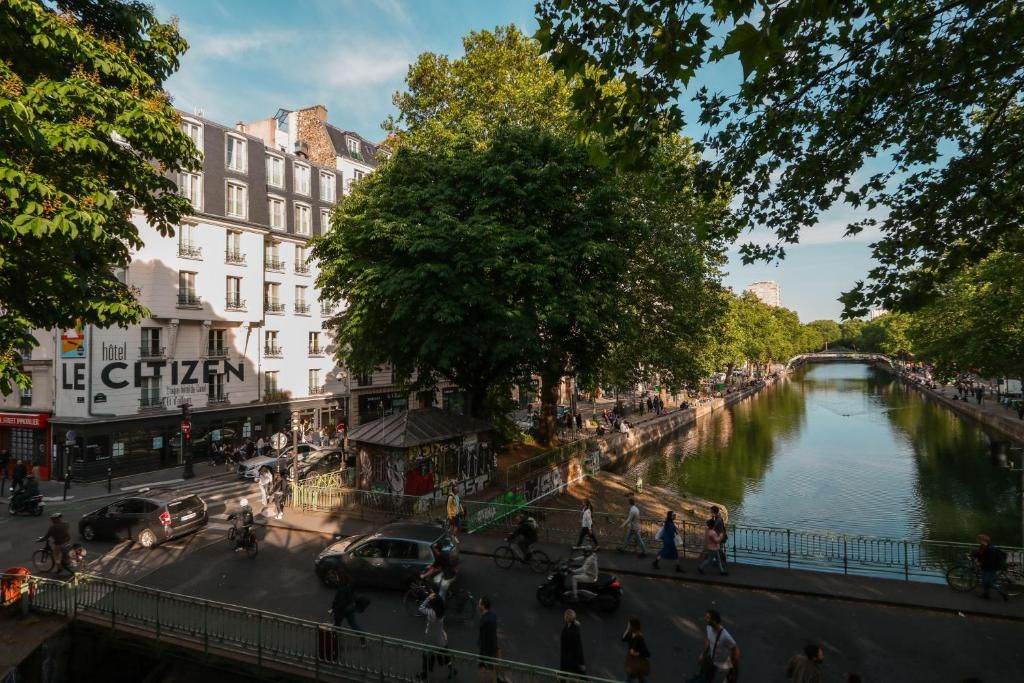People enjoy a sunny day along the canal in Amsterdam with historic buildings and trees lining the waterway.