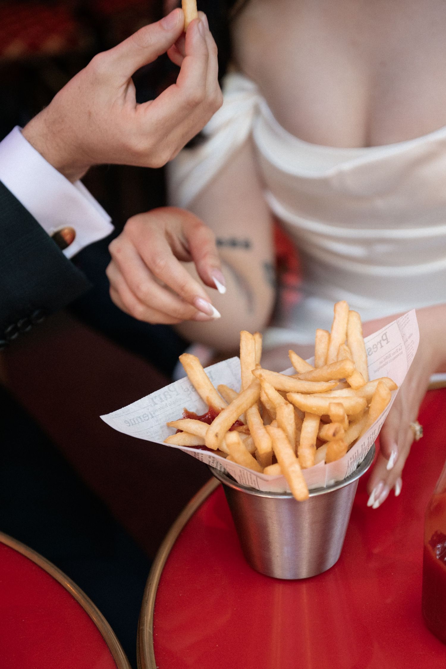 Golden french fries being served in a metal container on a red surface.