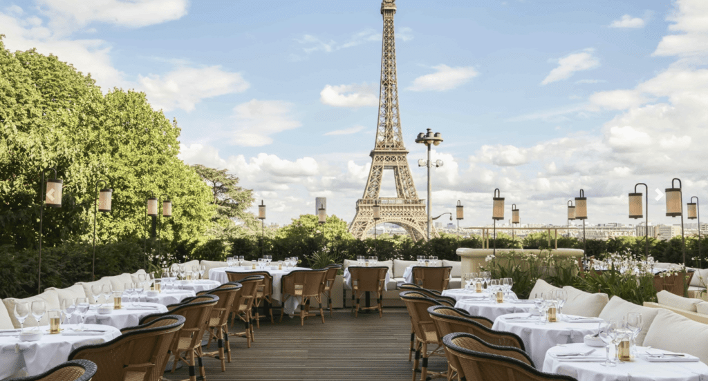 Rooftop restaurant with white tablecloths and Eiffel Tower view on sunny day.