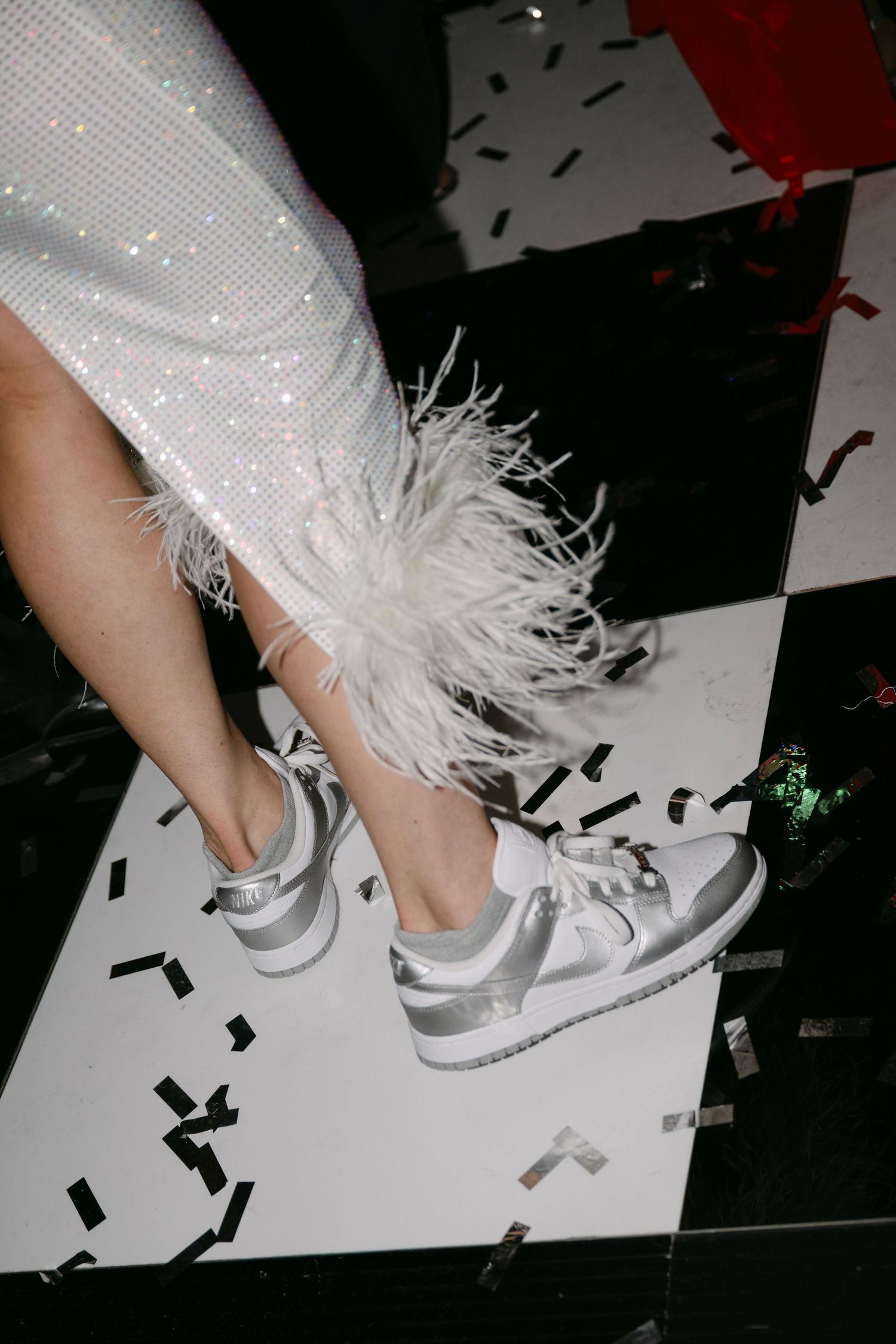 Close-up of silver sneakers with white feather trim on black and white checkered dance floor.