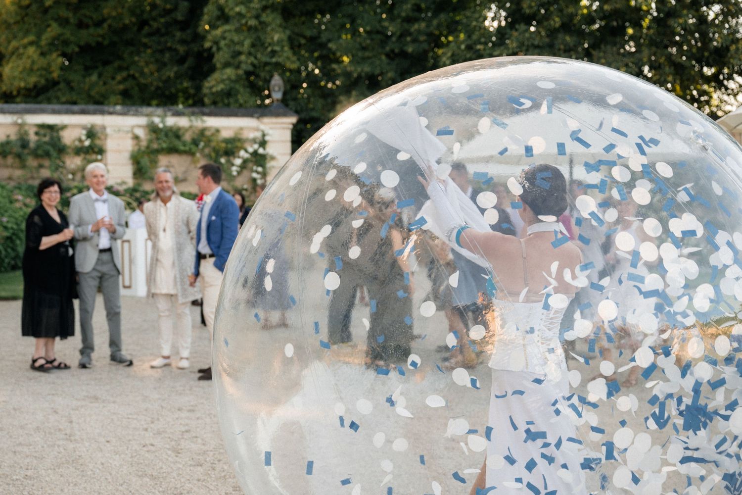 Wedding entertainer performing inside large transparent confetti-filled bubble sphere outdoors.