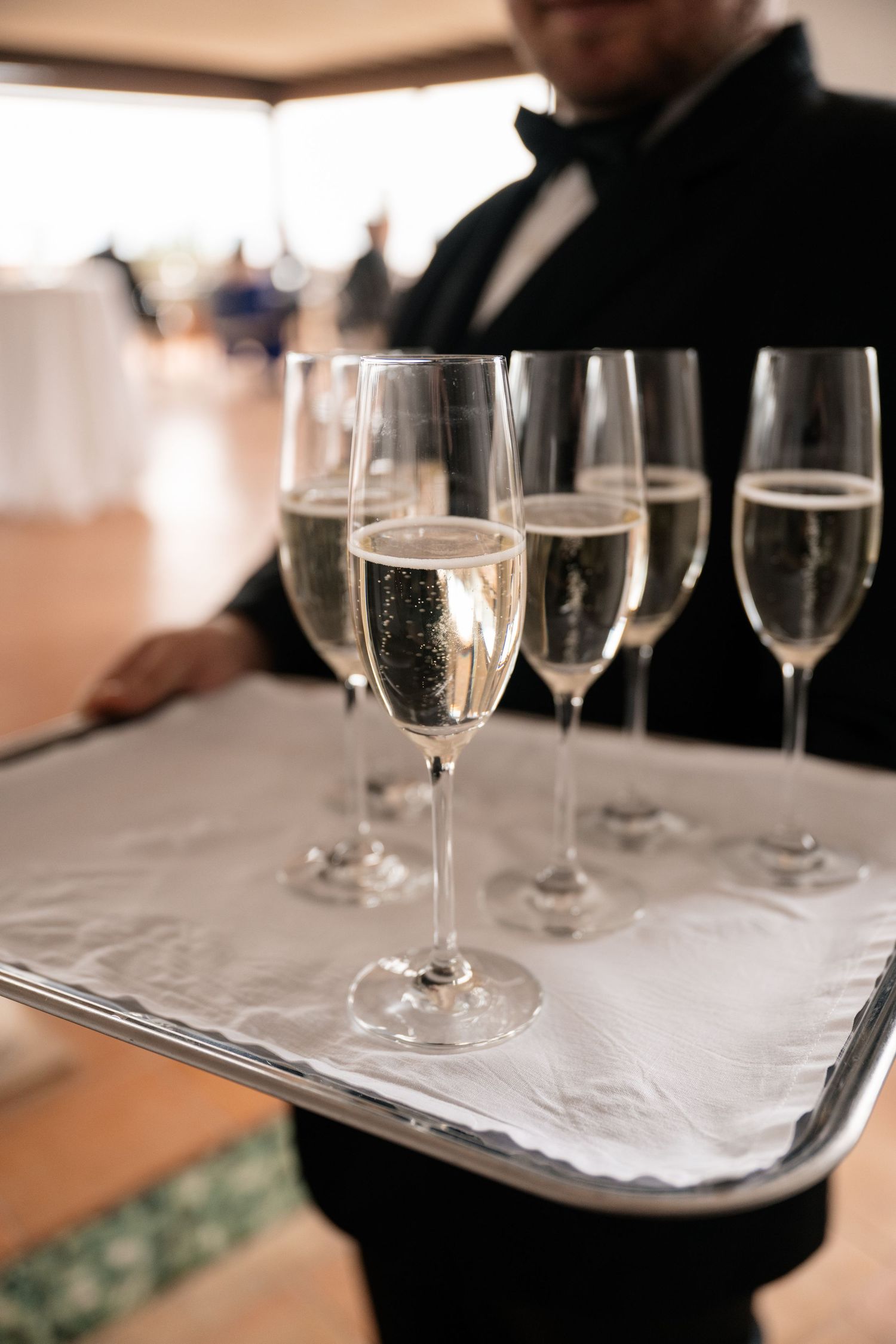 Formally dressed waiter serves champagne flutes on silver tray at elegant wedding reception.