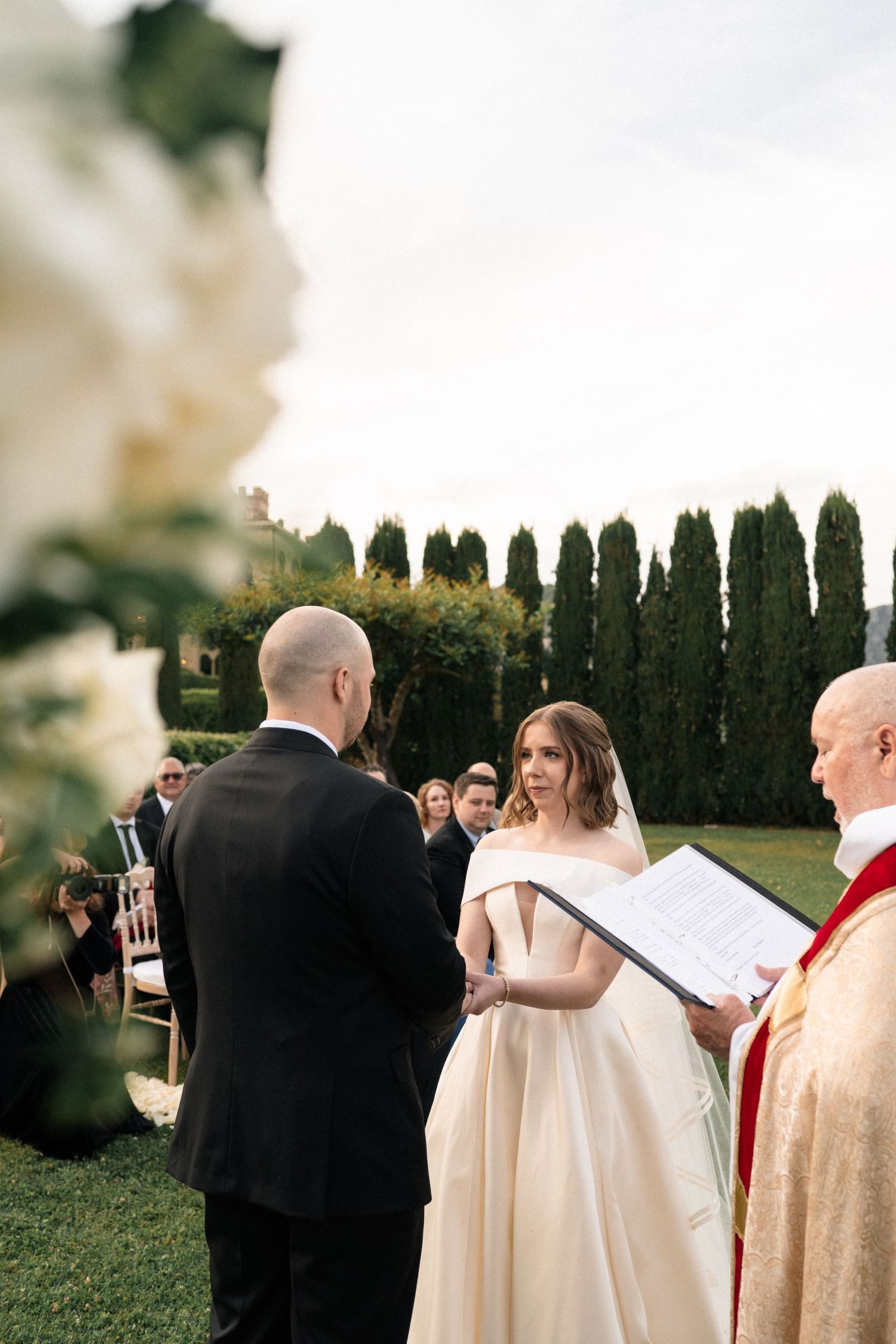 Bride reads vows to groom at elegant outdoor garden wedding ceremony in Italy.