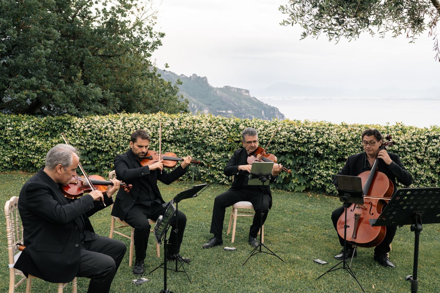 String quartet performs outdoors with stunning Amalfi Coast cliffside backdrop at elegant Italian wedding.
