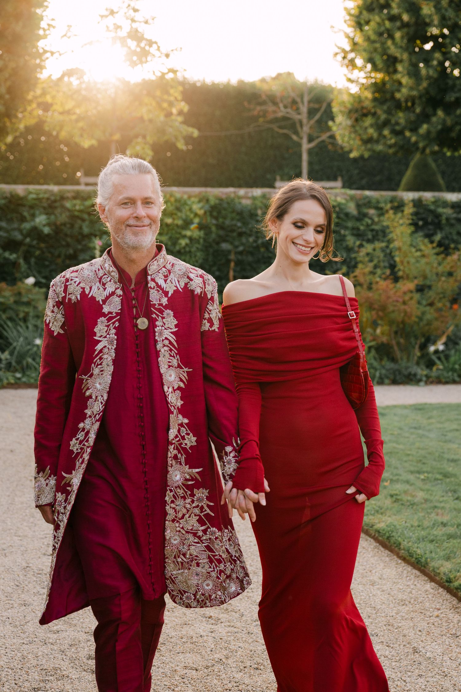Couple in matching red outfits walking hand in hand in a garden at golden hour.